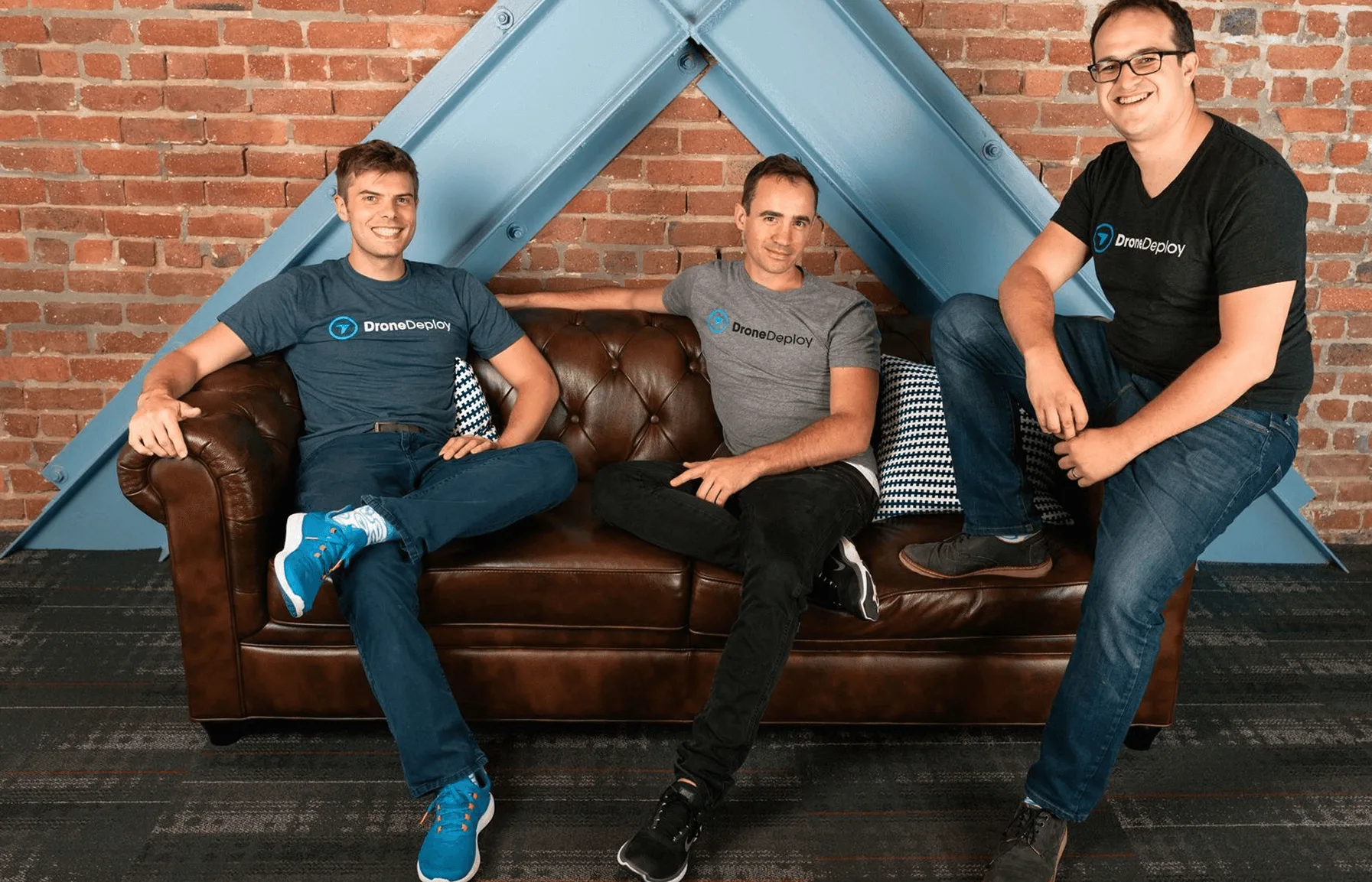 The three DroneDeploy founders in branded t-shirts sitting on a couch in their office.
