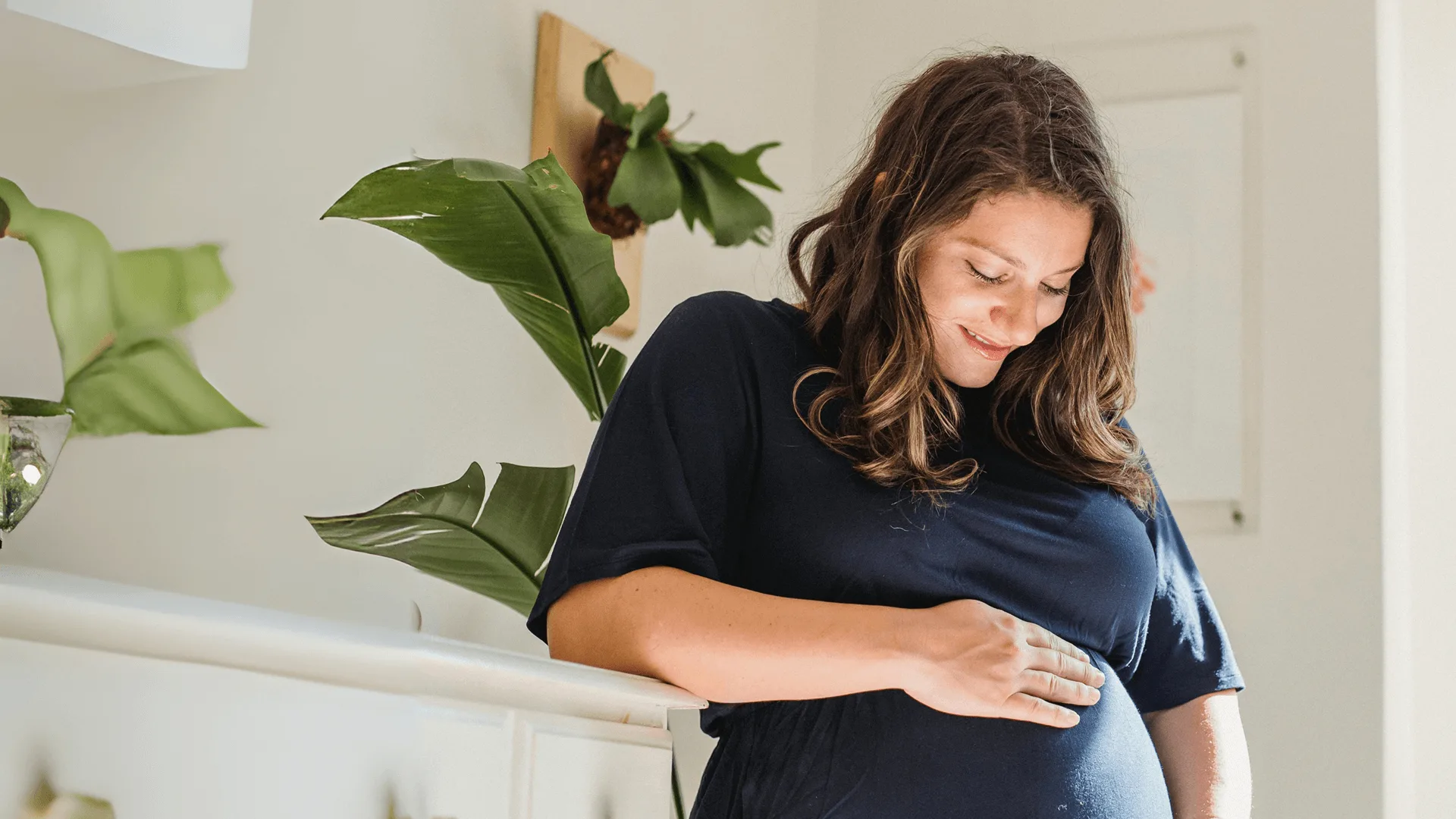 A pregnant woman resting a hand on her belly at home, for the Kindara fertility tracking app
