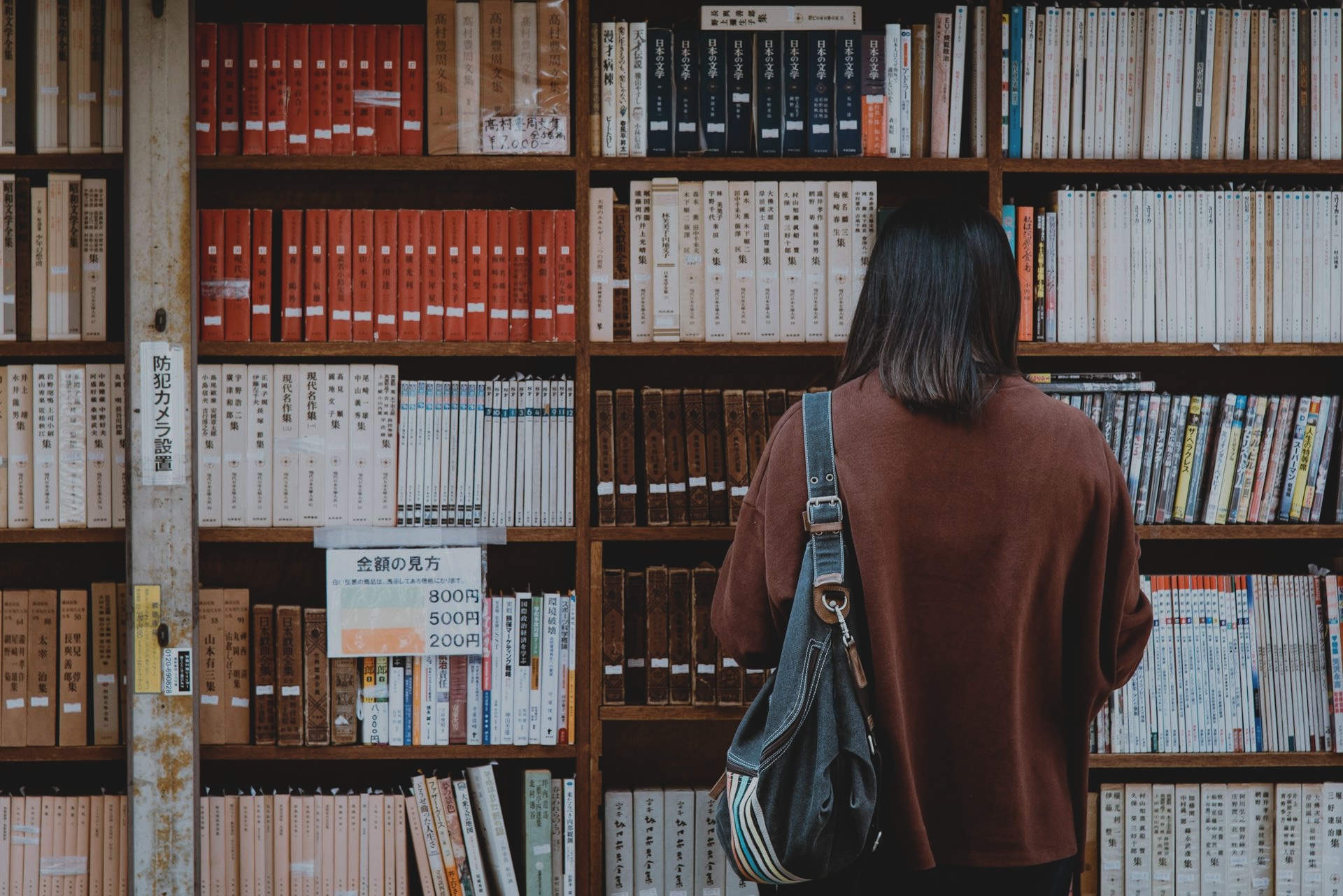 Woman wearing brown shirt carrying black leather bag on front of library books - Photo by Abby Chung via Pexels.com