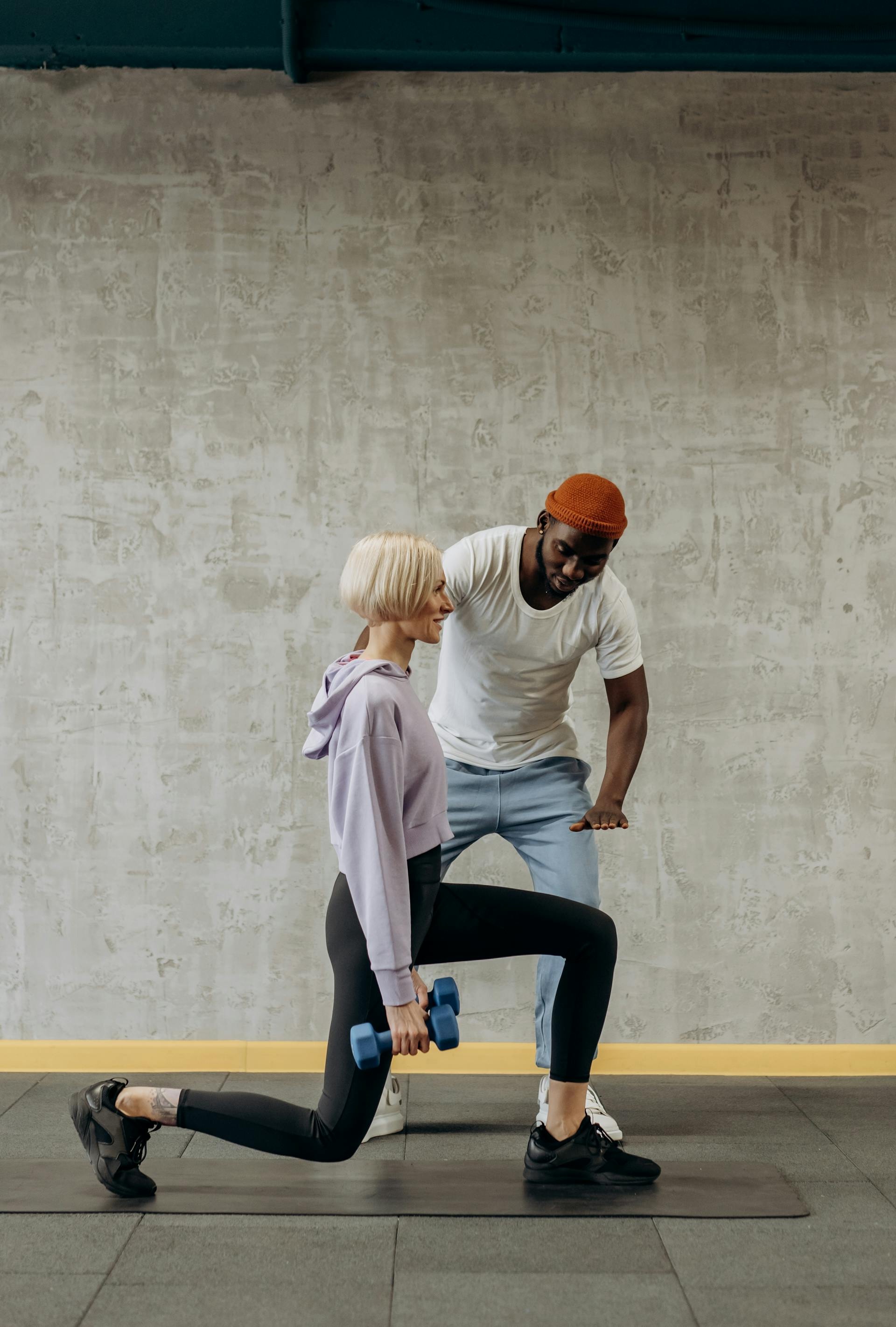 A personal trainer guides a woman doing lunges with dumbbells in a gym setting. Fitness and lifestyle concept.