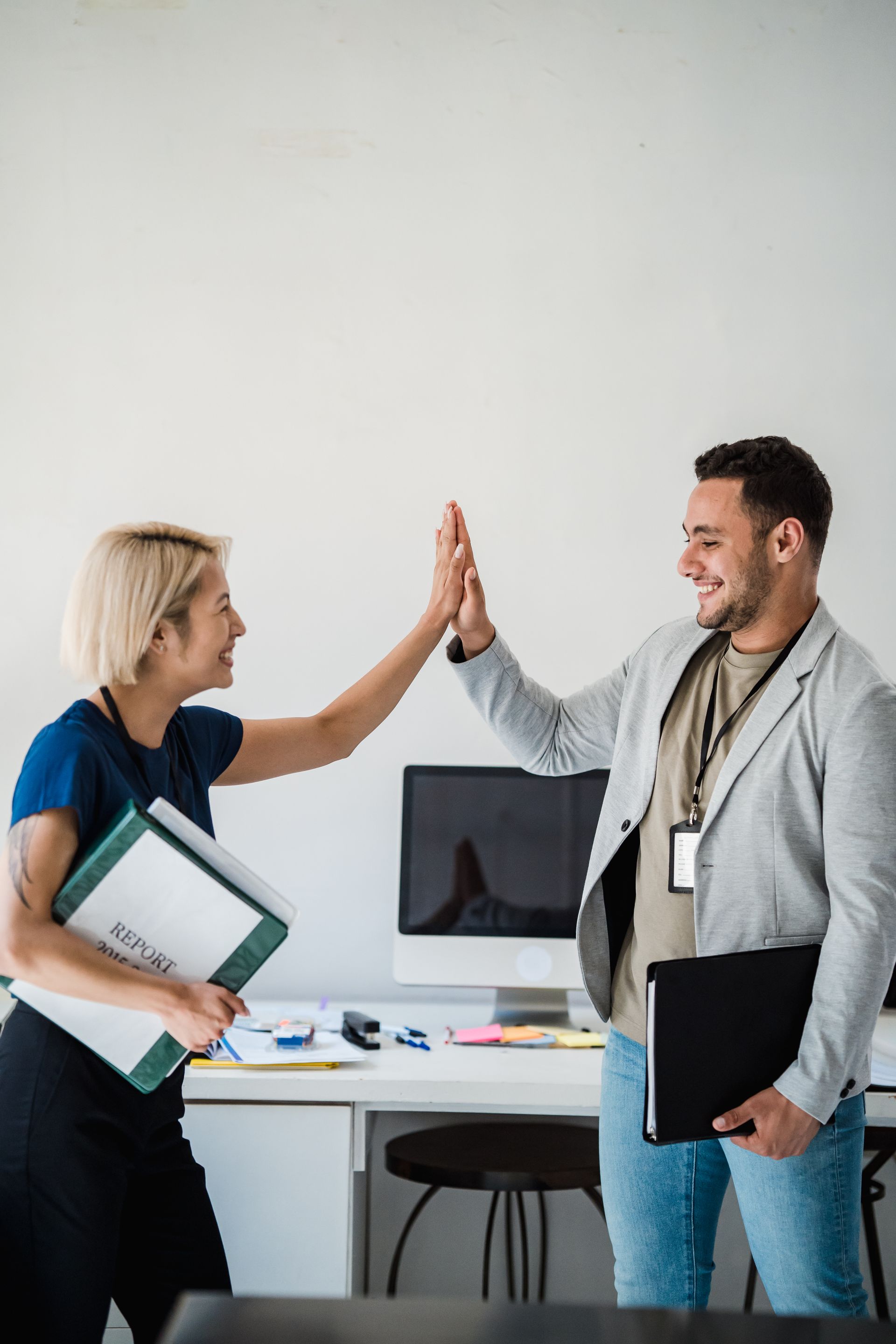 Two colleagues share a high-five in a modern office setting, showcasing teamwork and success. Photo by Mizuno K via Pexels.com