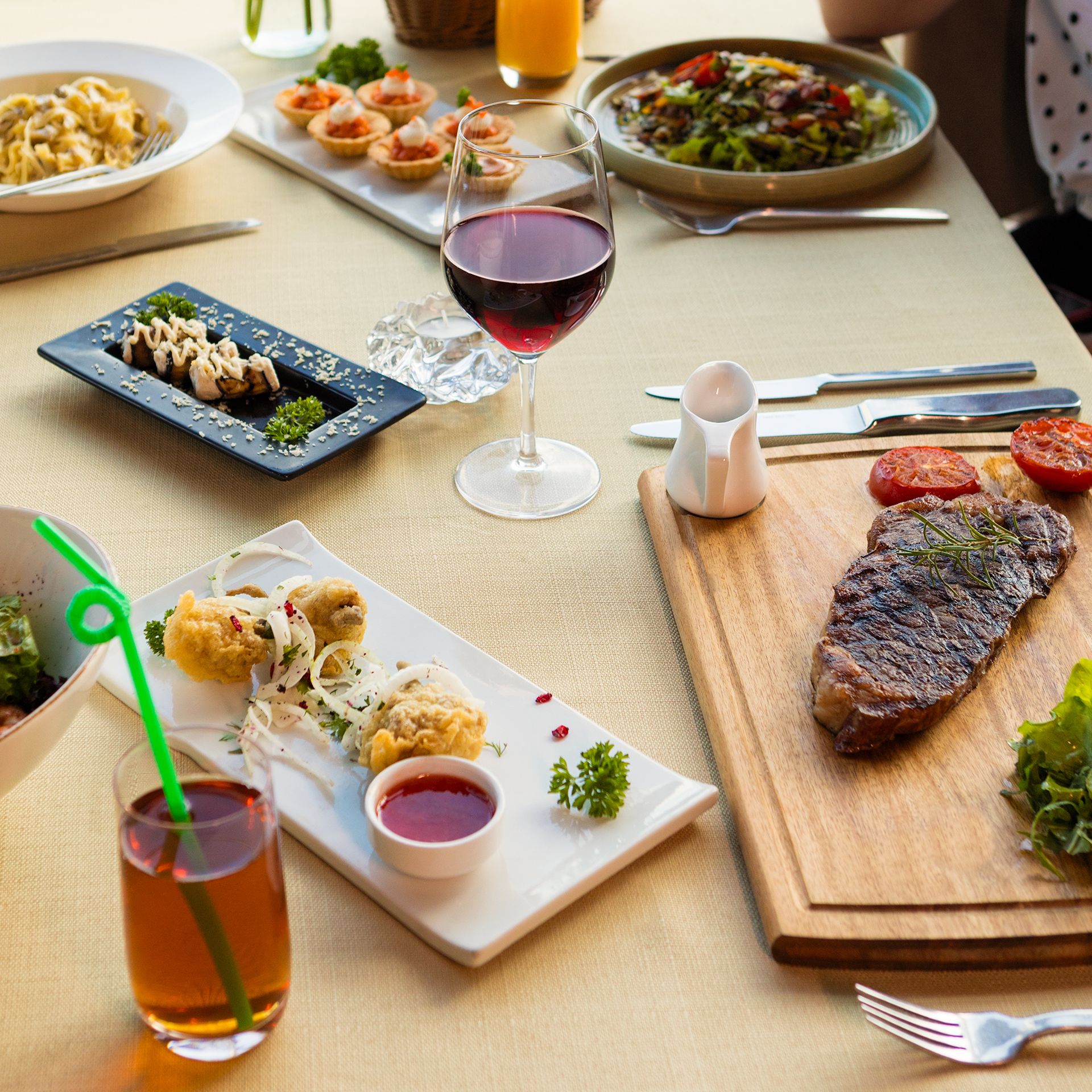 A lavish meal spread with steak, red wine, and various appetizers on a neatly set table. Photo by Farhad Ibrahimzade, via Pexels.com