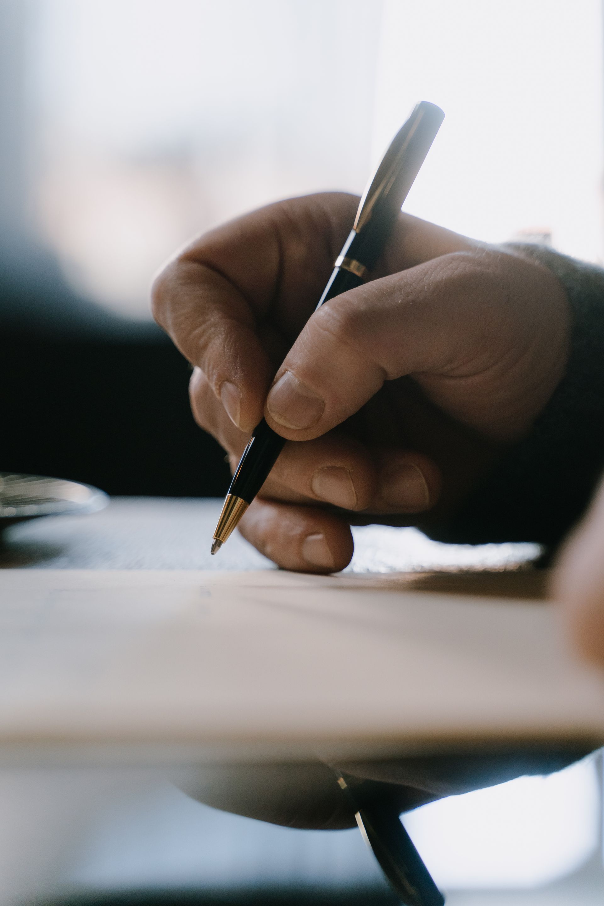 Detail shot of a hand holding a pen, writing on paper with blurred background. Photo by cottonbro studio, via Pexels.com