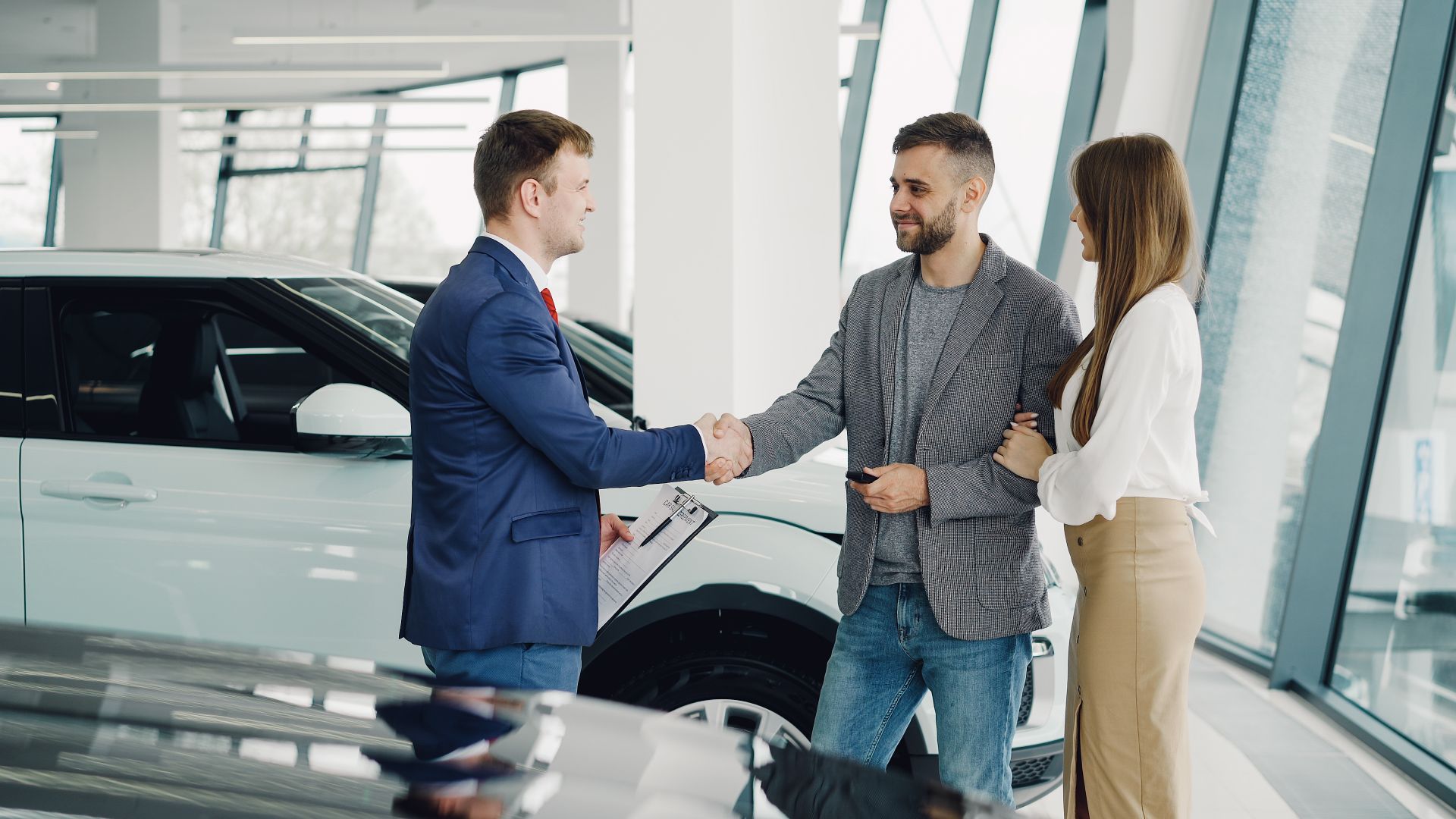 A couple completes a transaction with a salesman at a modern car dealership. Photo by Vitaly Gariev, via Pexels.com