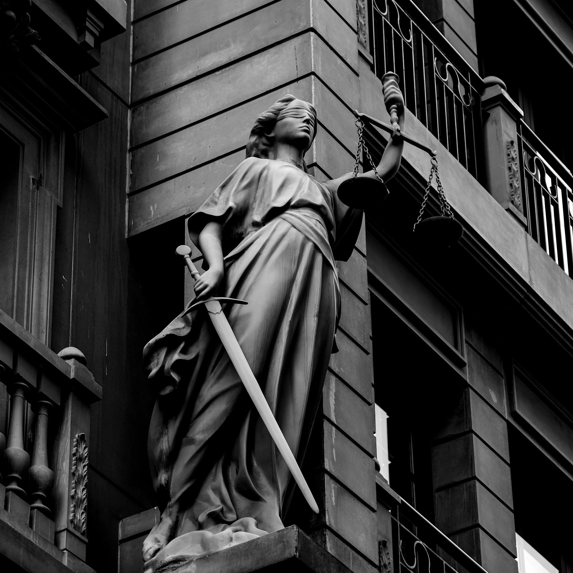 A dramatic black and white photo of a justice statue holding a sword and scales. Photo by Furkan Alakoç via Pexels.com