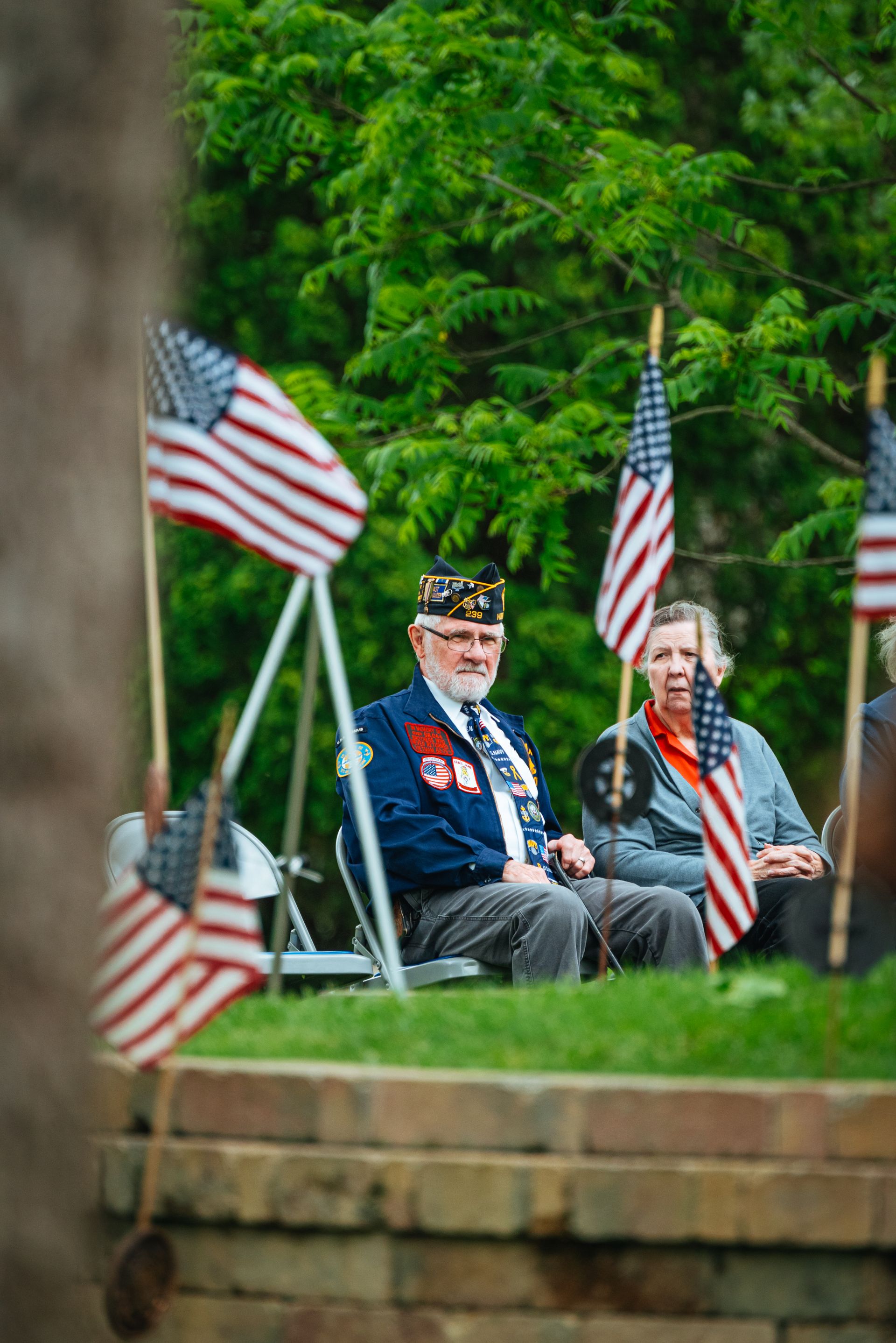Elderly veterans sitting among American flags at an outdoor ceremony. Photo by Chris F via Pexels.com