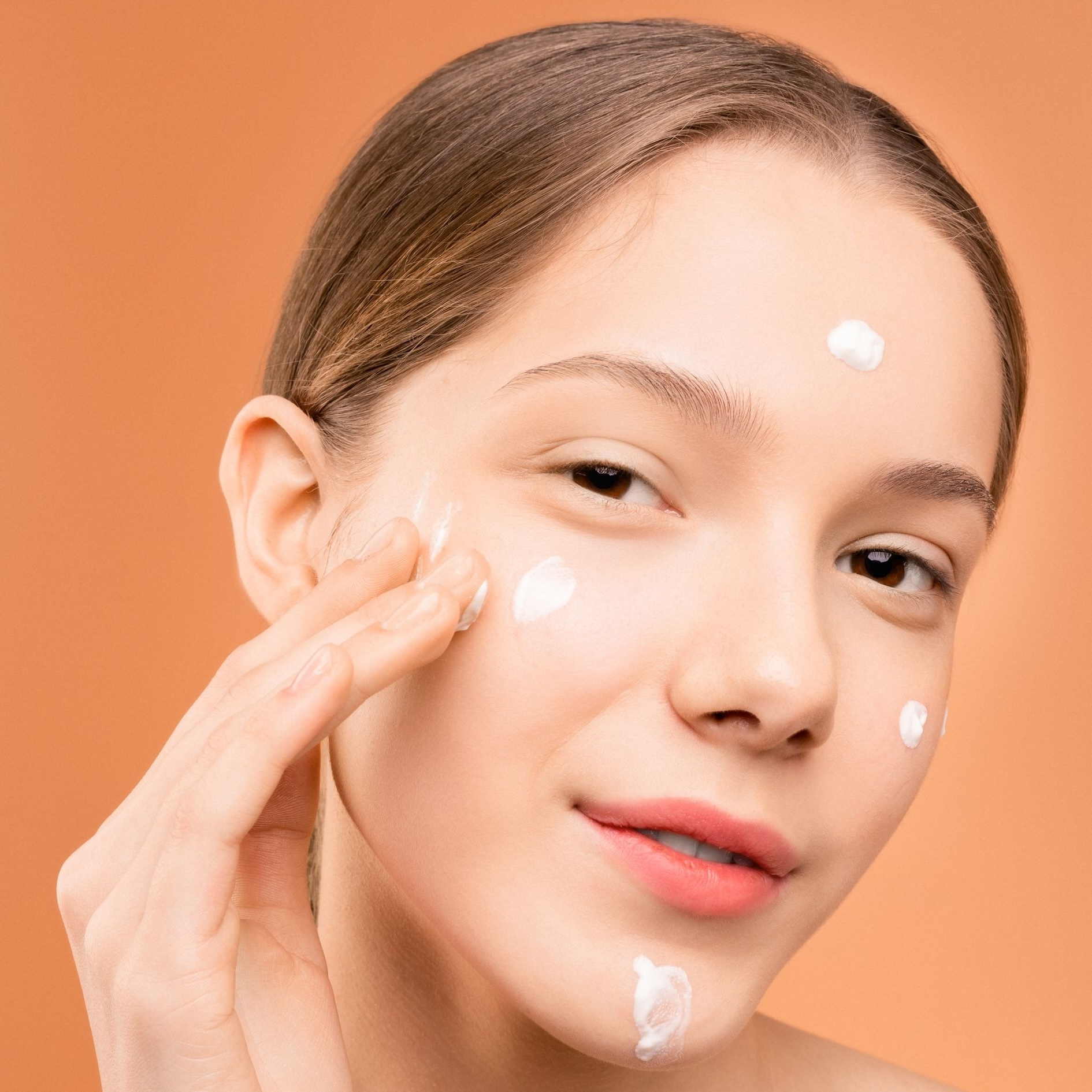Close-up of a young woman applying facial moisturizer with a serene expression. Photo by Shiny Diamond via Pexels.com