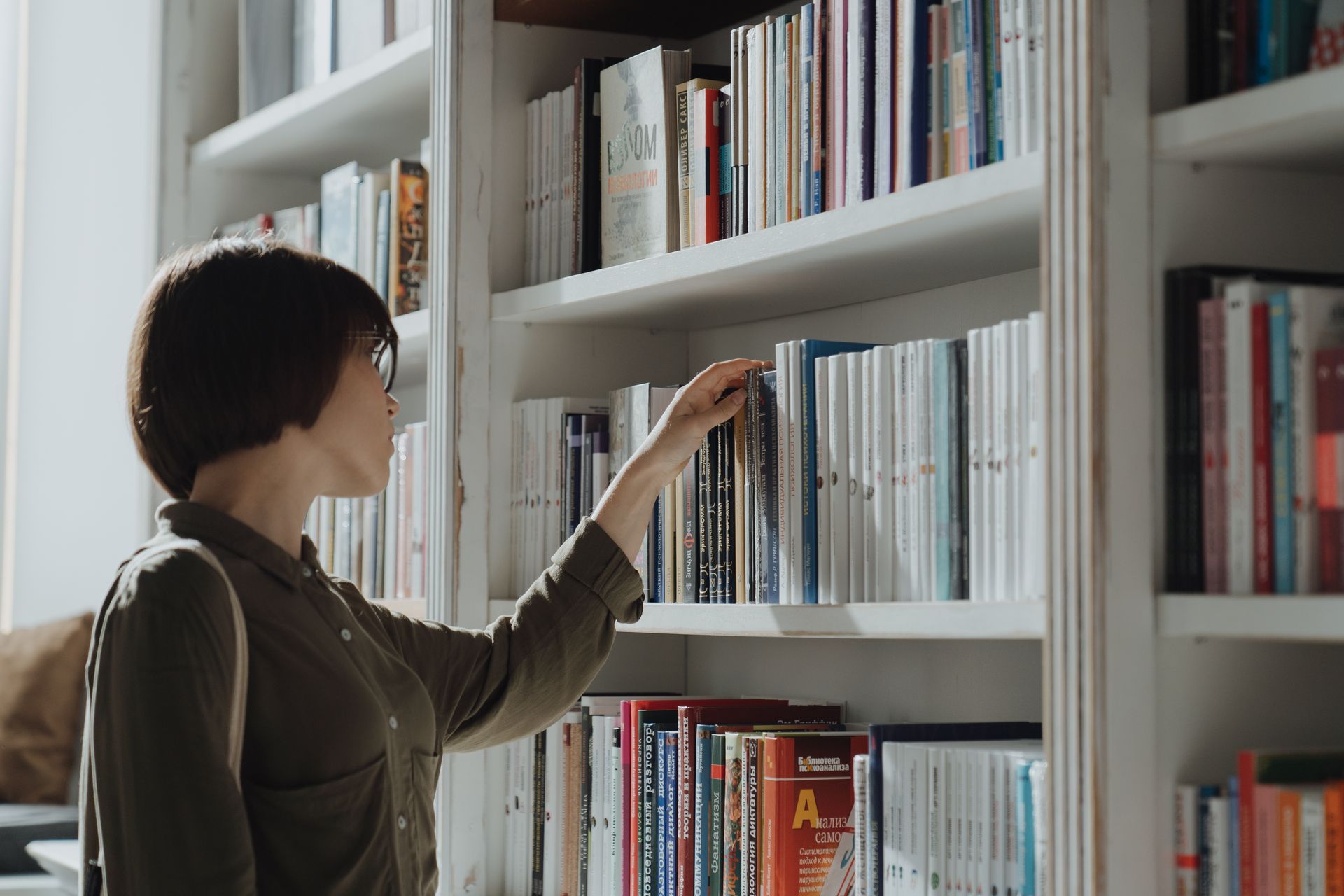 A woman browsing a bookshelf in a modern library setting, exploring various literature options. Photo by cottonbro studio via Pexels.com