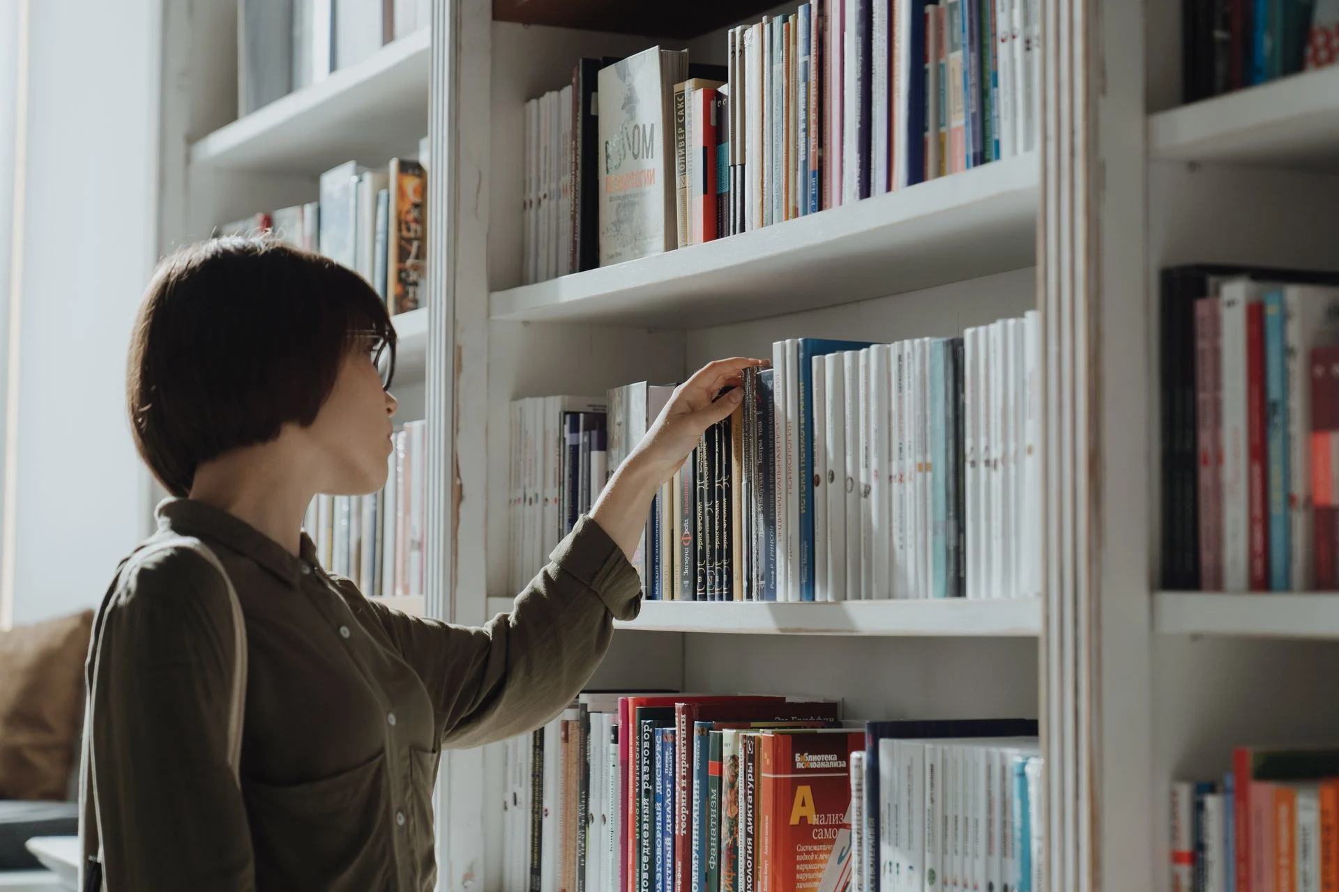 A woman browsing a bookshelf in a modern library setting, exploring various literature options. Photo by cottonbro studio via Pexels.com