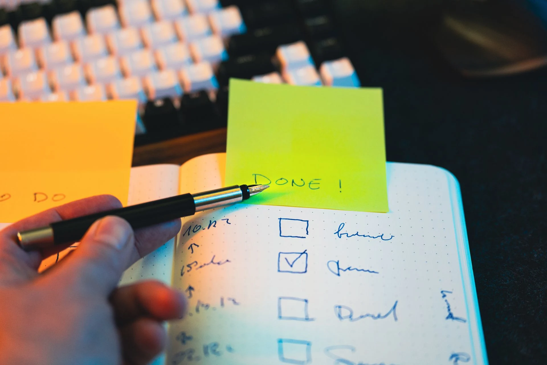 Close-up of hand holding pen over notebook checklist with sticky notes labeled 'DONE!'. Photo by Jakub Zerdzicki via Pexels.com
