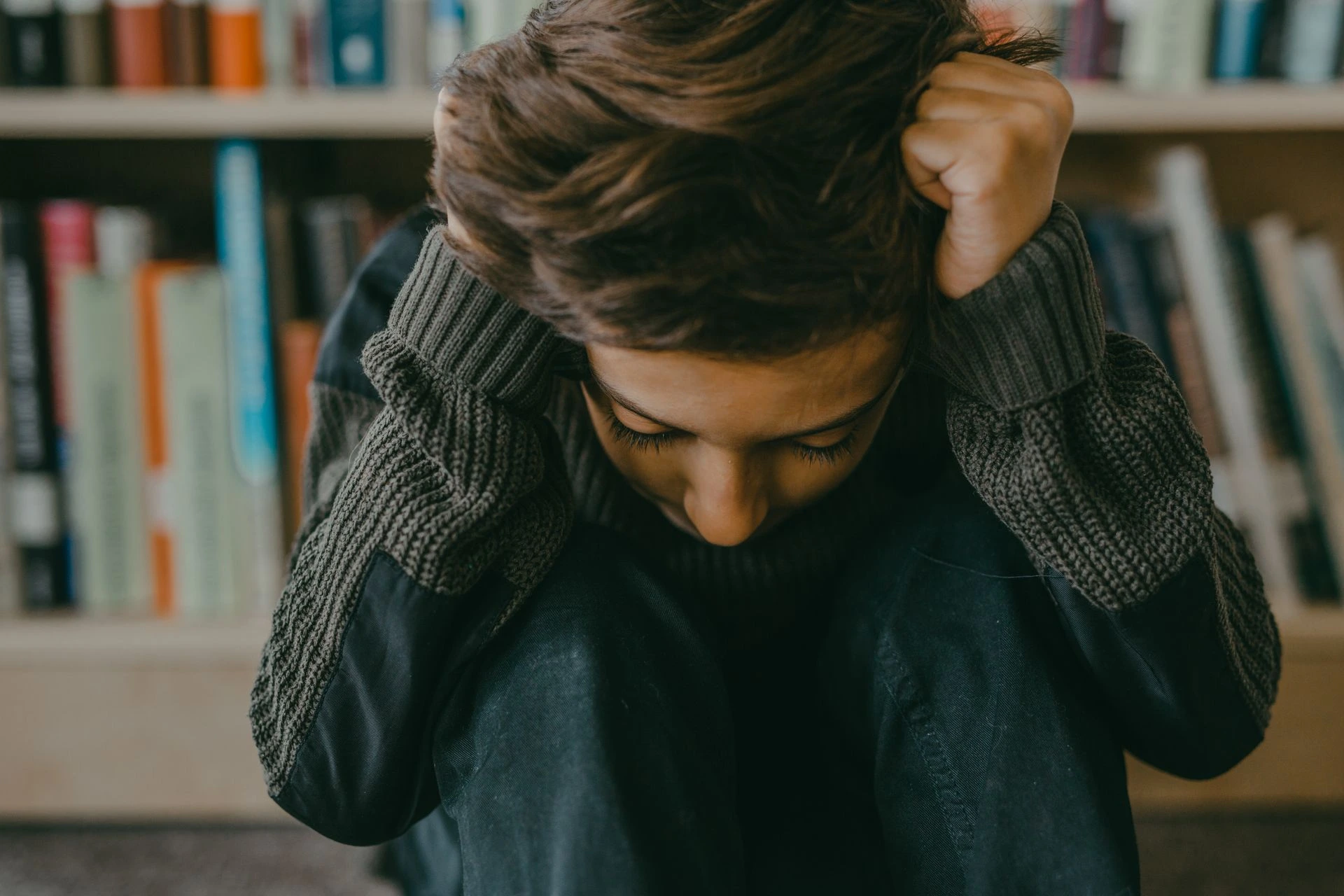A young person sitting in a thoughtful, introspective pose in a library setting. Photo by Mikhail Nilov via Pexels.com