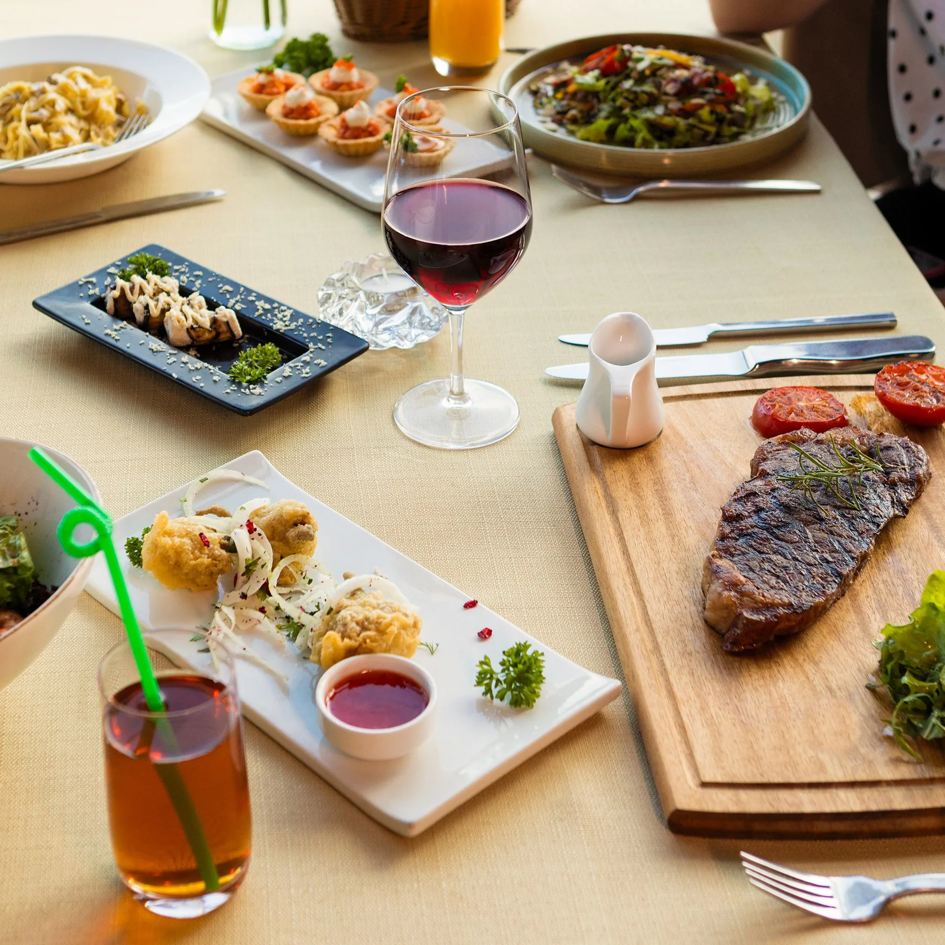 A lavish meal spread with steak, red wine, and various appetizers on a neatly set table. Photo by Farhad Ibrahimzade, via Pexels.com