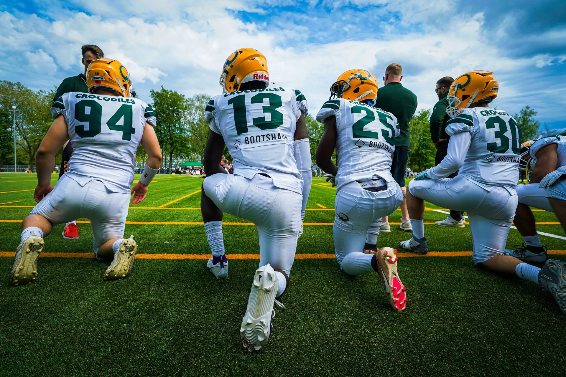 A group of American football players wearing helmets and sports gear kneeling on a green field. Photo by Darku, via Pexels.com