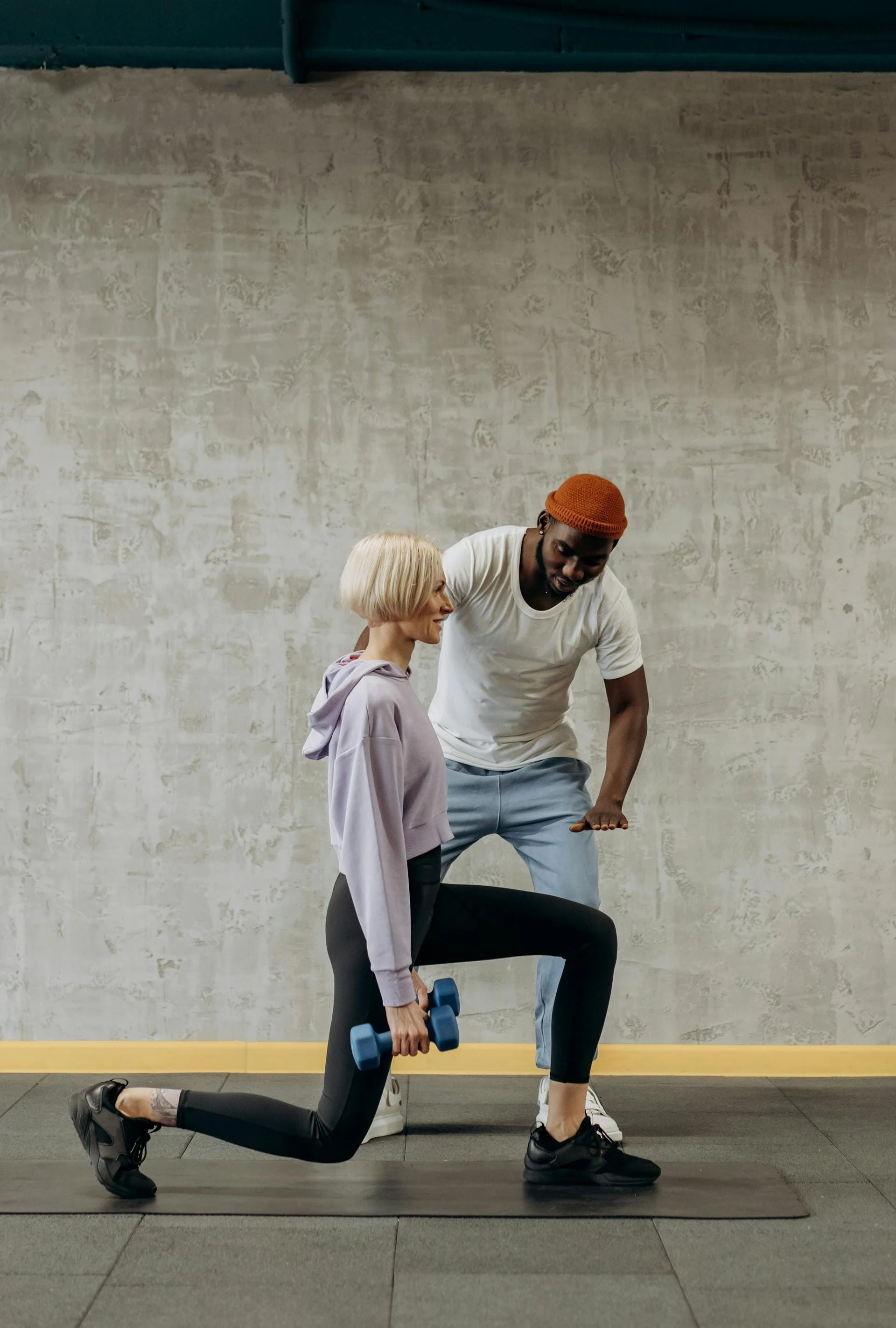 A personal trainer guides a woman doing lunges with dumbbells in a gym setting. Fitness and lifestyle concept.