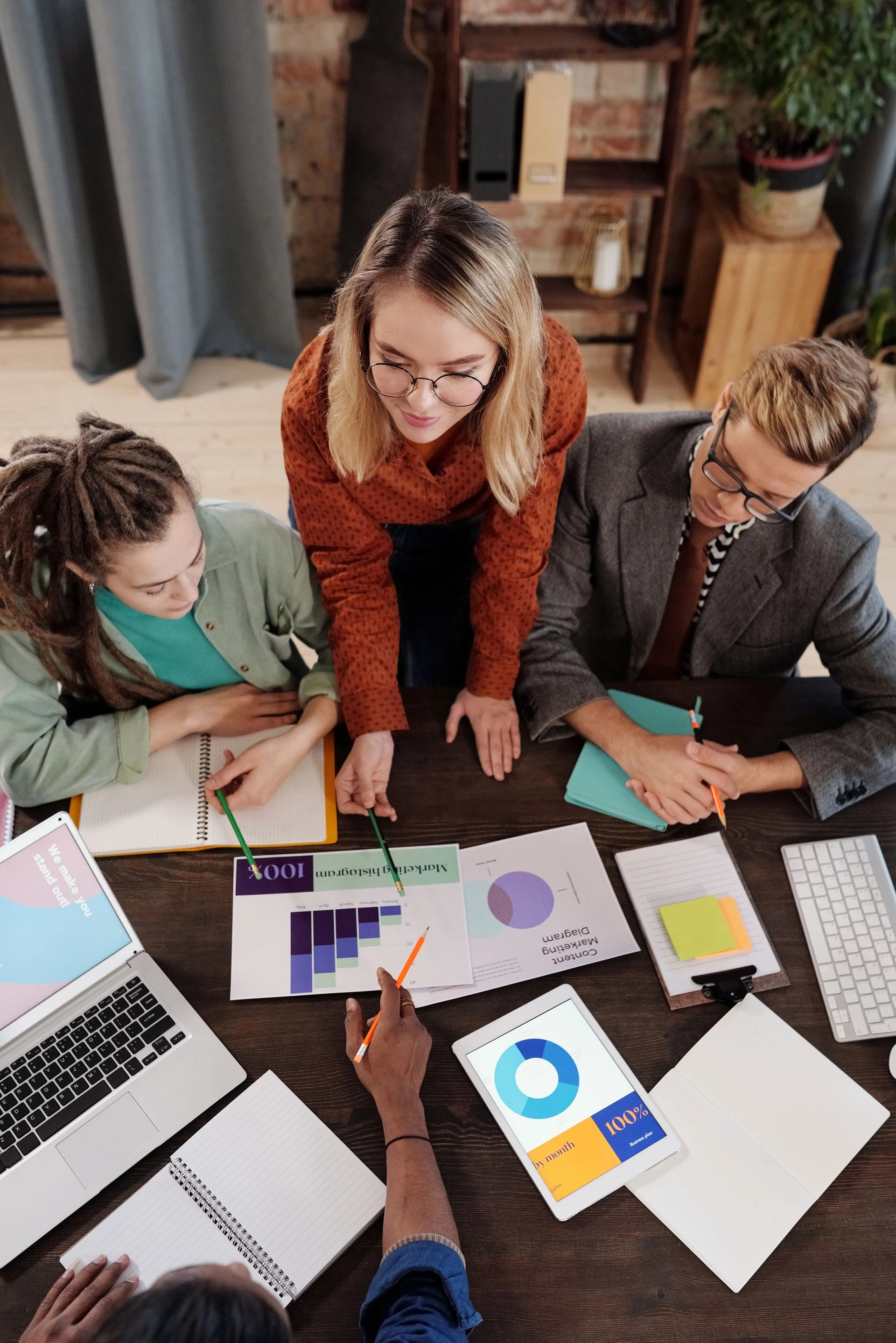 Top view of a diverse group discussing business reports and charts around a desk. Photo by Mikael Blomkvist via Pexels.com