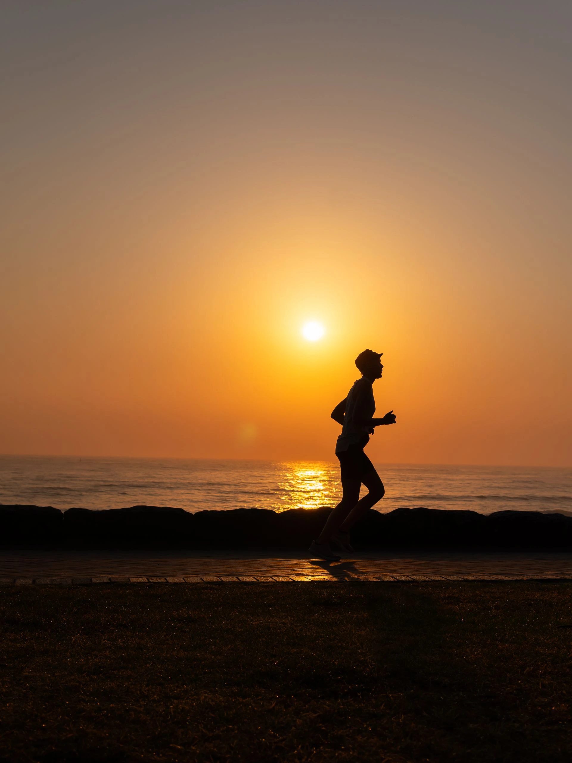 A silhouette of a person running along the ocean shore during a picturesque sunset. Photo by Talha Resitoglu via Pexels.com