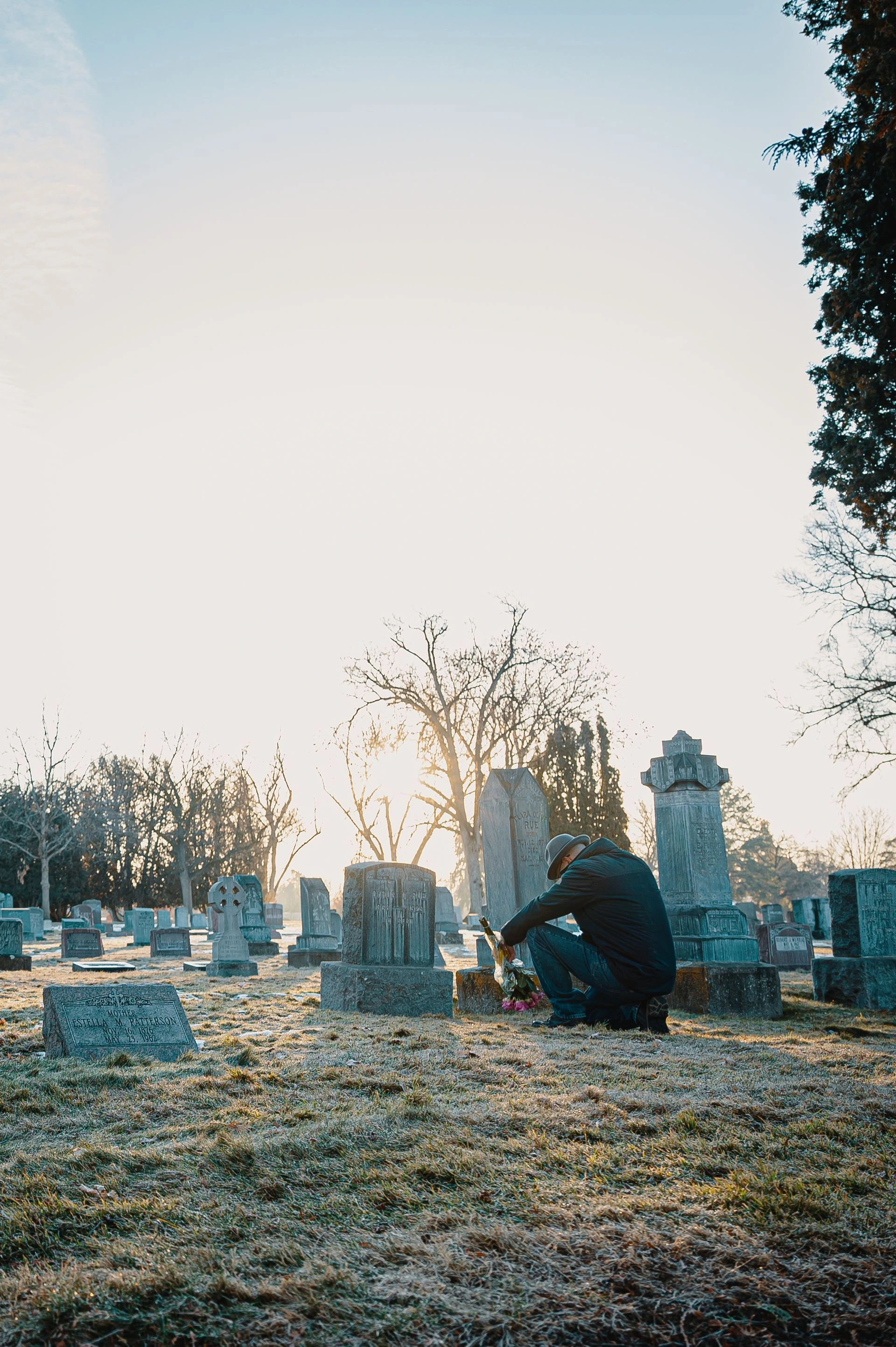 A person kneeling by a grave in a peaceful cemetery during a serene winter day. Photo by Brett Sayles via Pexels.com