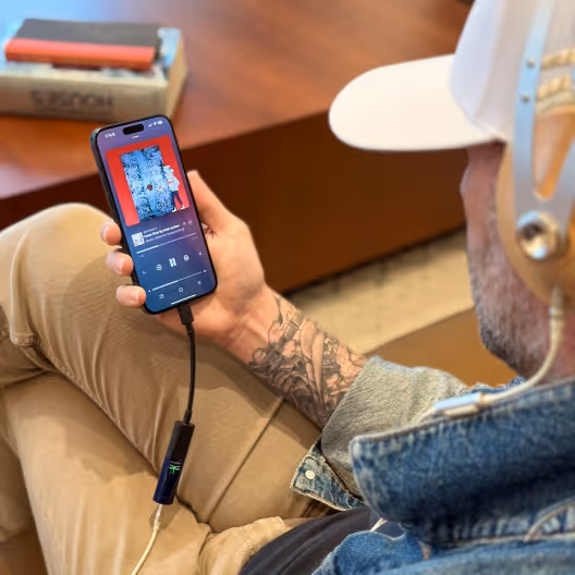 Person wearing headphones holding smartphone playing a podcast with visible album art and controls.