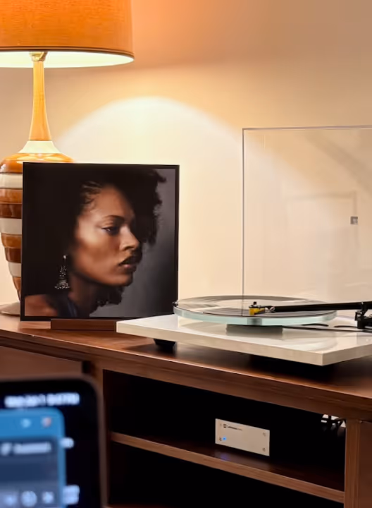 Record player on wooden cabinet next to a lamp and a framed profile portrait of a woman with curly hair.