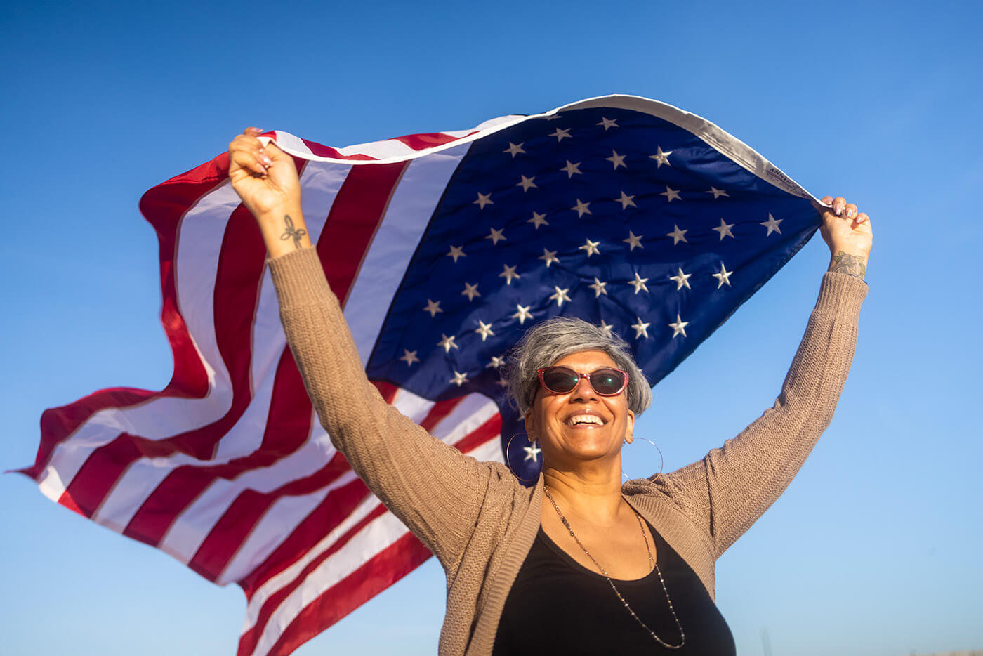 A happy black woman carrying and waving an American Flag at the beach.