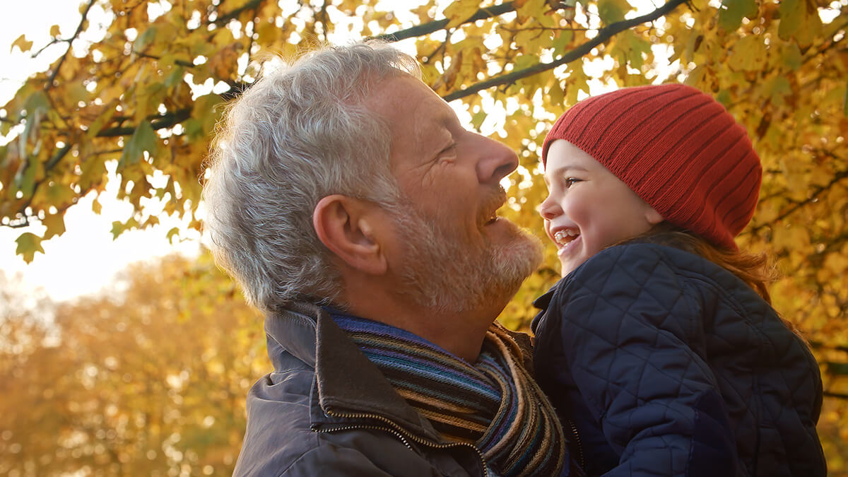 Happy Grandfather Holding Granddaughter While Smiling Outdoors