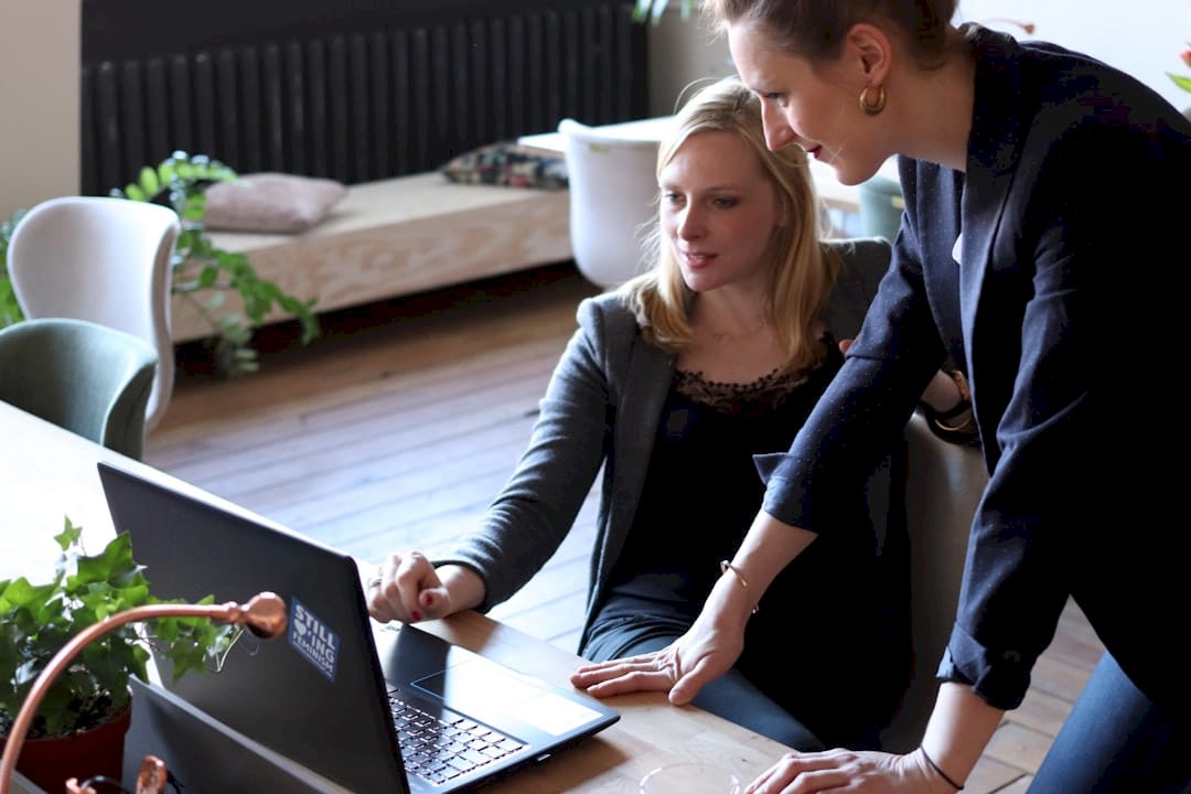 two women looking at a laptop on a table