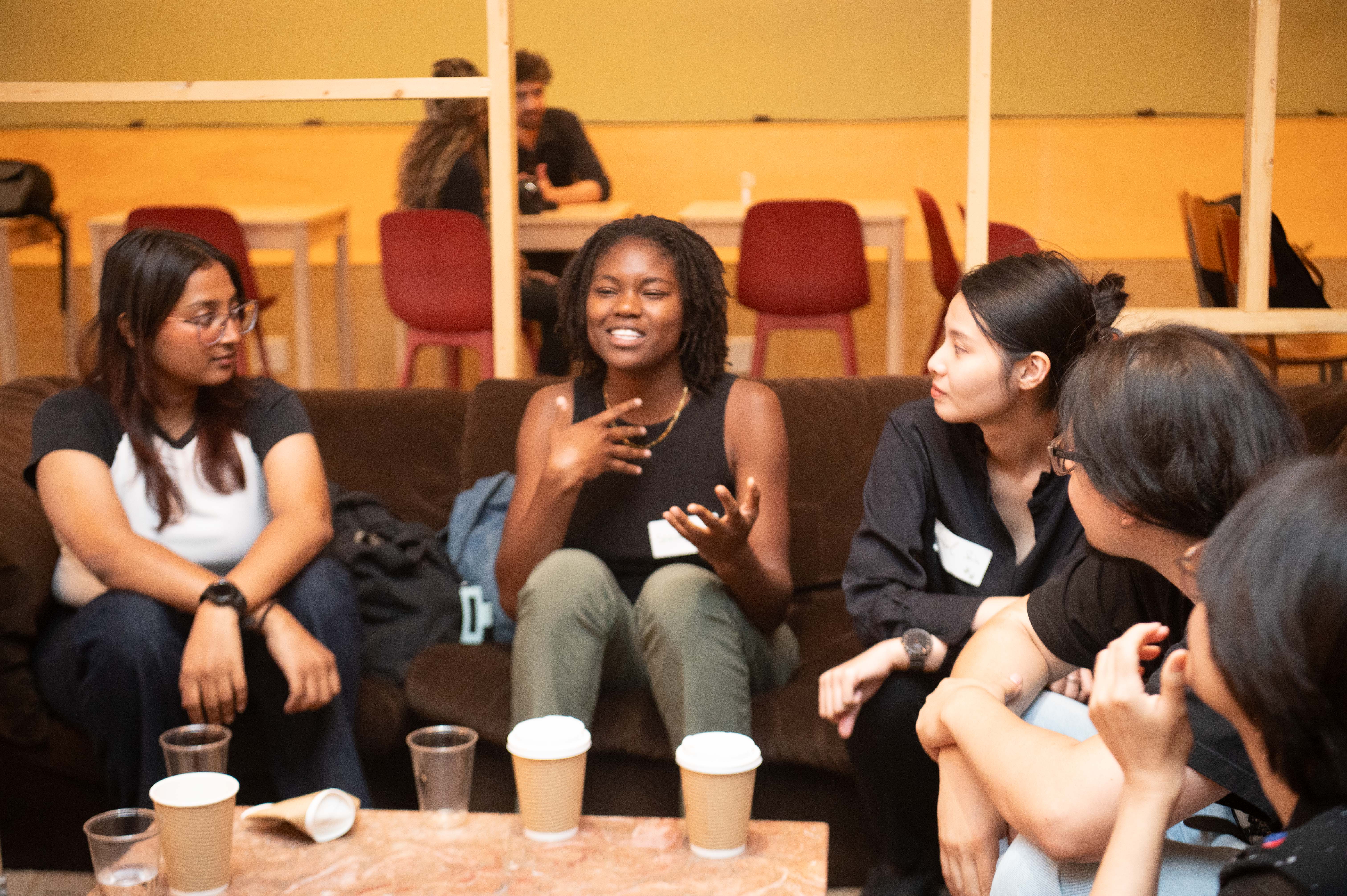 Workshop scene: a girl stands presenting her sticky notes, as four peers with laptops sit and listen.