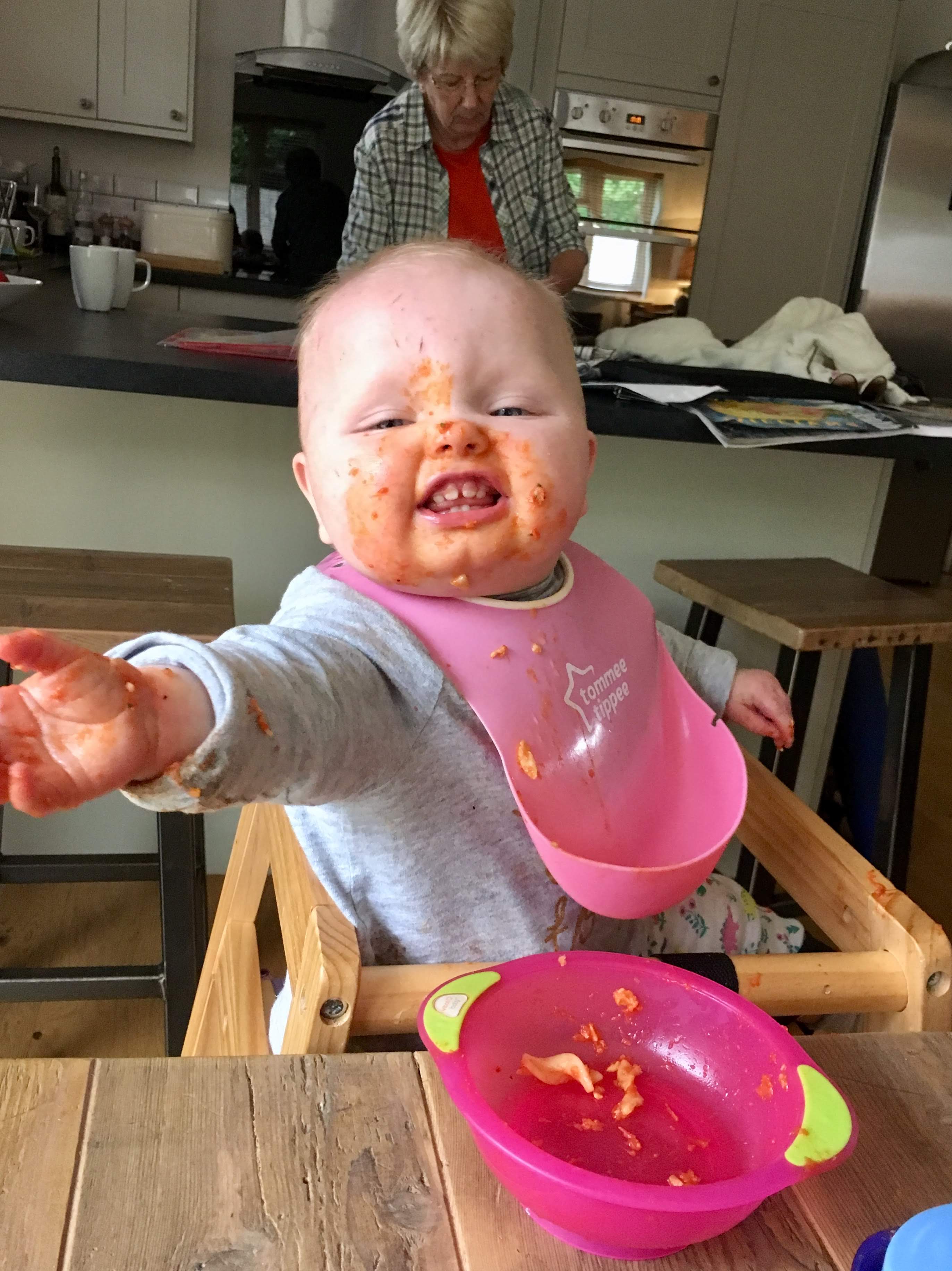 Baby covered in food sits and enjoys her dinner at child-friendly Gwelmor self catering holiday cottage in north Cornwall