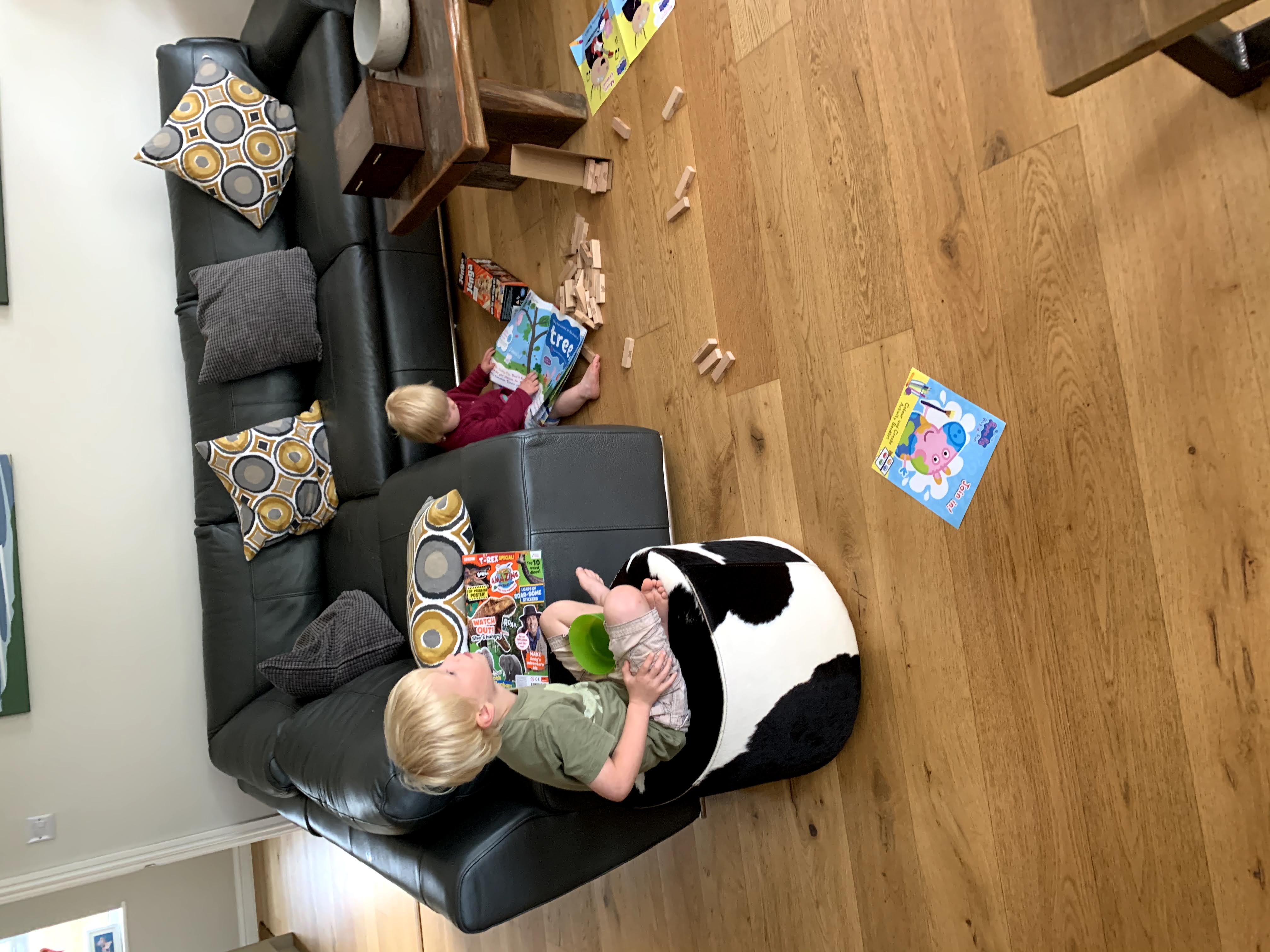 Child sits on poof whilst watching television while younger sibling plays on the floor in spacious Gwelmor, a child-friendly self-catering holiday cottage in north Cornwall