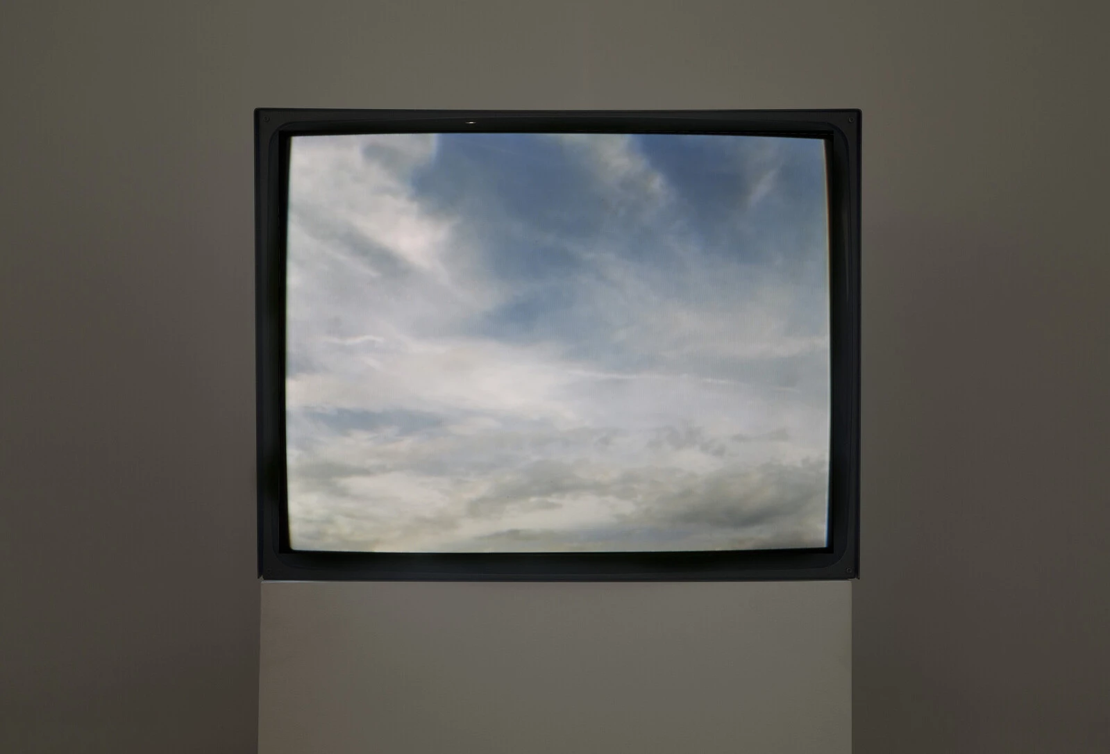 A dark room with a black frame on a pedestal featuring a view of wispy clouds
