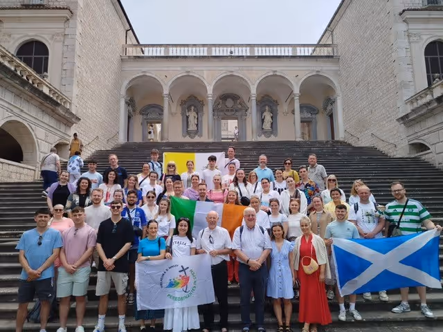 Around 60 young teachers are shown posing on a huge flight of steps in Rome, some holding flags - Scottish, Irish, Vatican and Jubilee of Hope