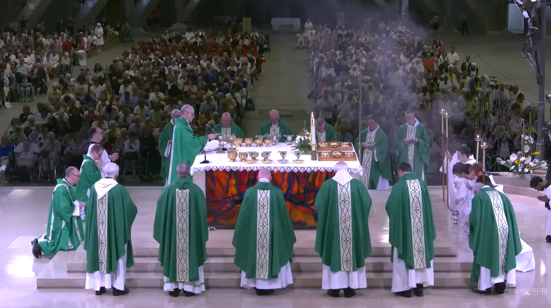 Thousands of lay faithful can be seen behind the huge altar in the Underground Basilica, around which ten bishops are gathered.