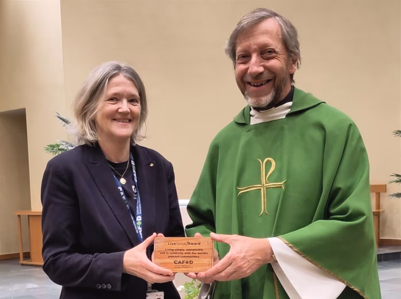 Jenny and Canon Rob are pictured holding a small wooden plaque engraved with Cafod and livesimply.