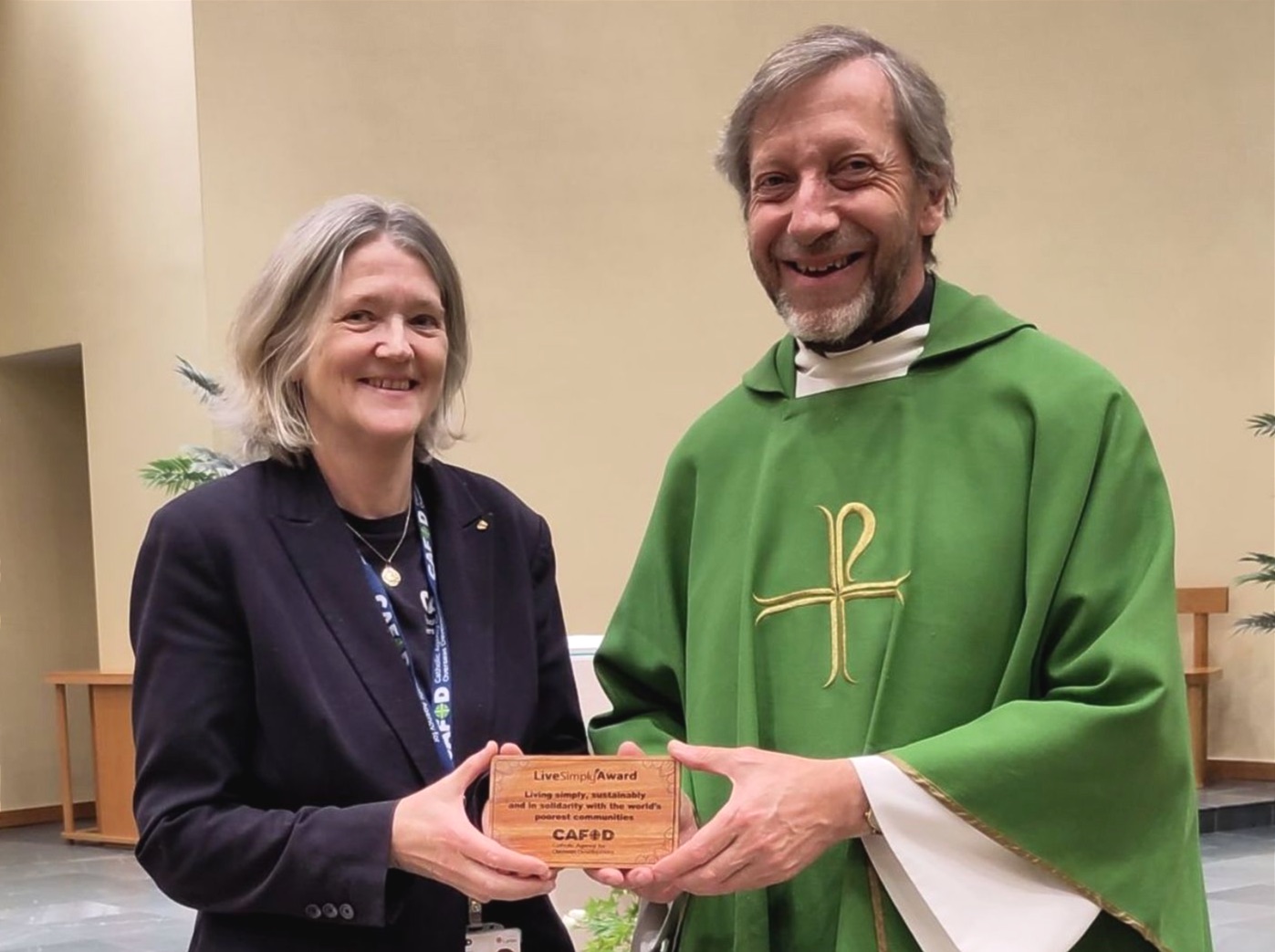 Jenny and Canon Rob are pictured holding a small wooden plaque engraved with Cafod and livesimply.