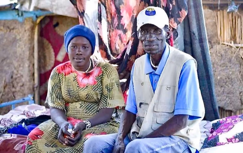 Two people, a man and a woman are seen sitting on a bed.