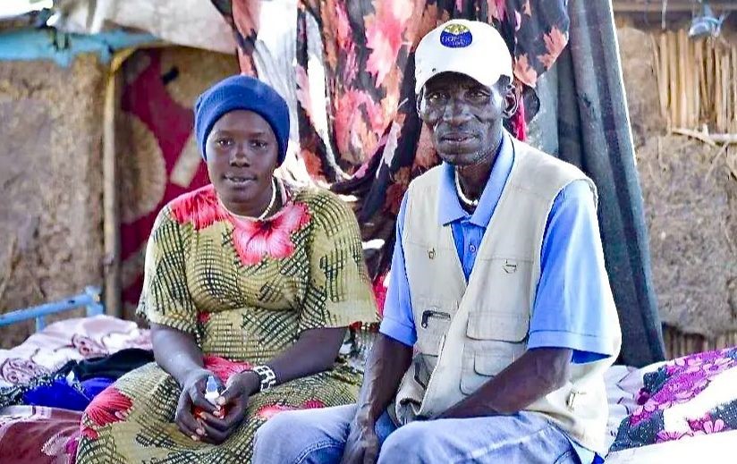 Two people, a man and a woman are seen sitting on a bed.