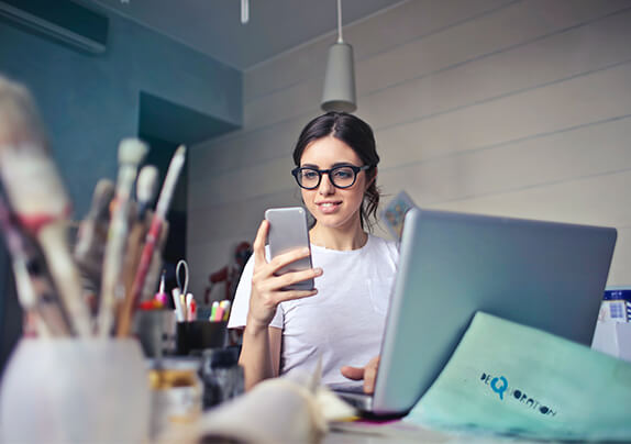 A imagem mostra uma moça em seu escritório realizando seu trabalho por meio de um celular. Um retrato comum de muitos brasileiros empreendedores.