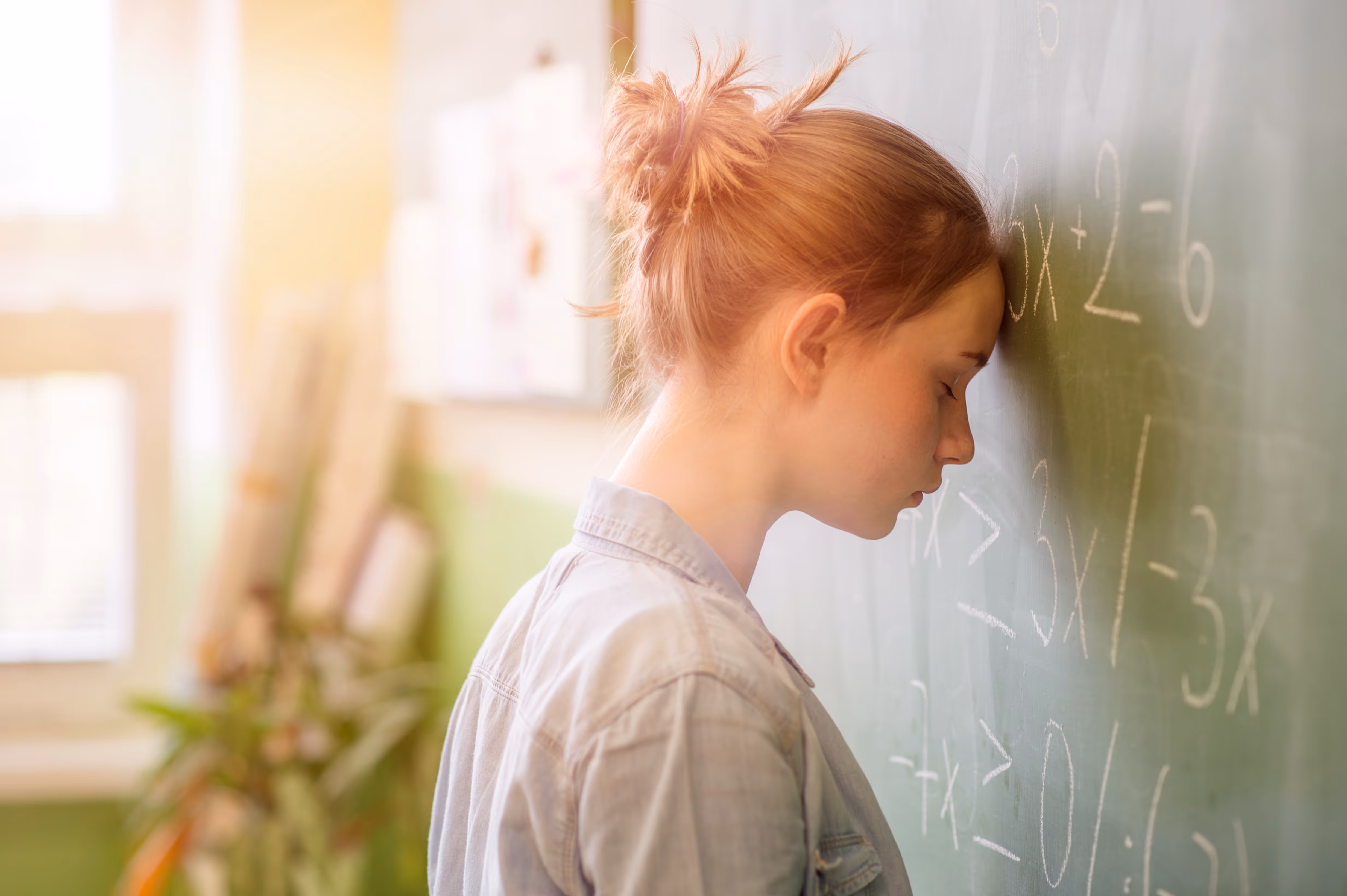A girl with a ponytail and a blue shirt is leaning against a chalkboard.