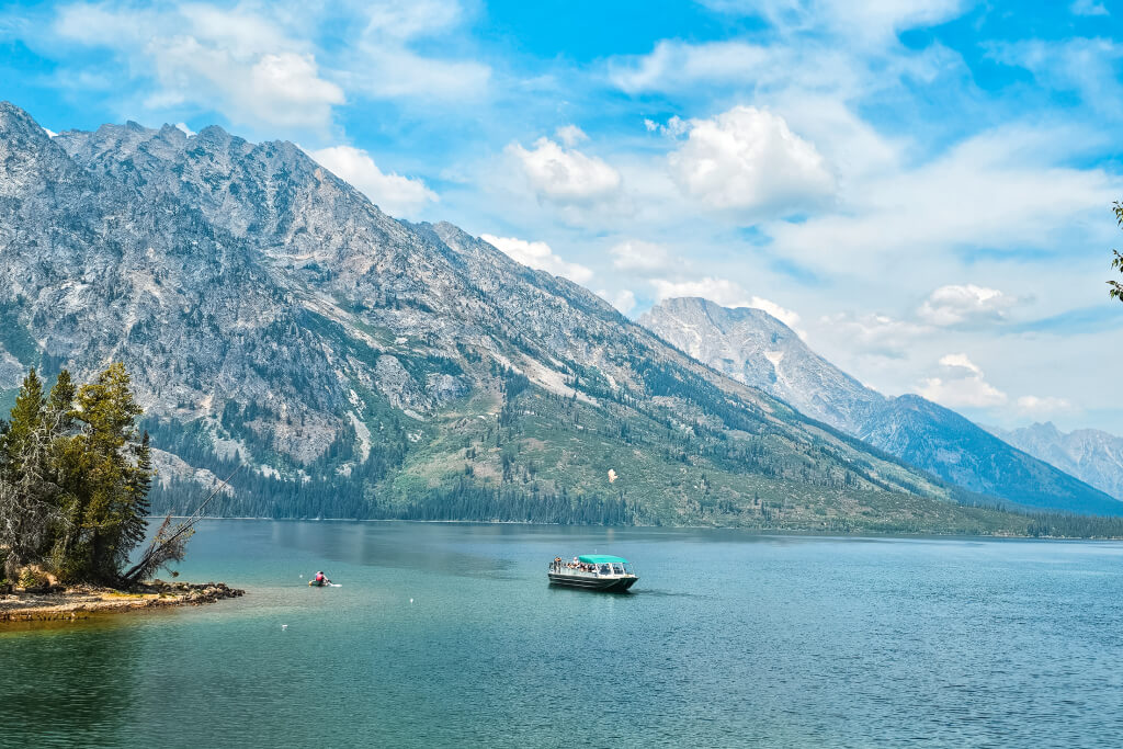 a boat on a crystal blue lake surrounded by mountains in Grand Teton