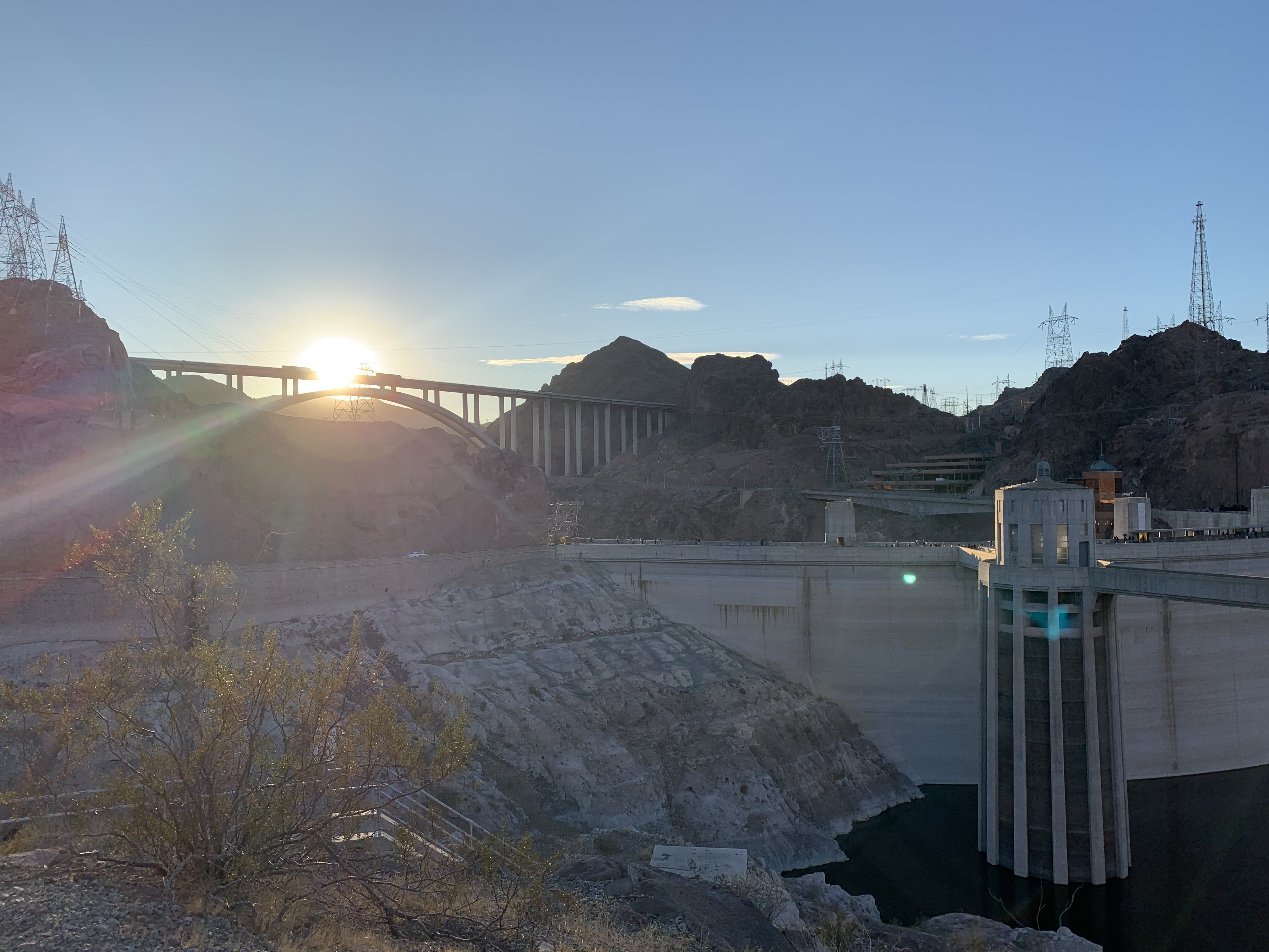 A view of a bridge by the Hoover Dam with the sunlight shining in the background.