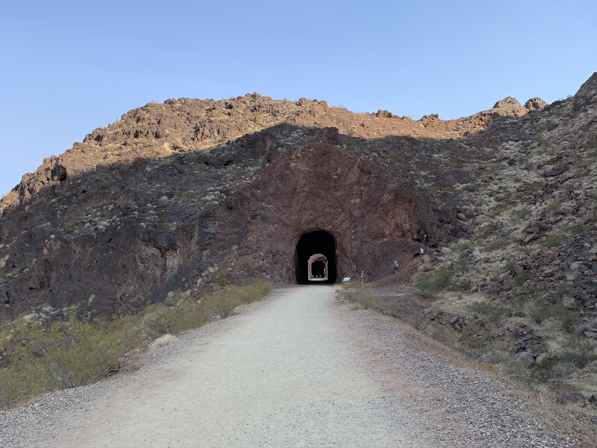A view of a railroad tunnel built in a canyon by Lake Lake. There is a path leading through the tunnel for hikers to hike through.