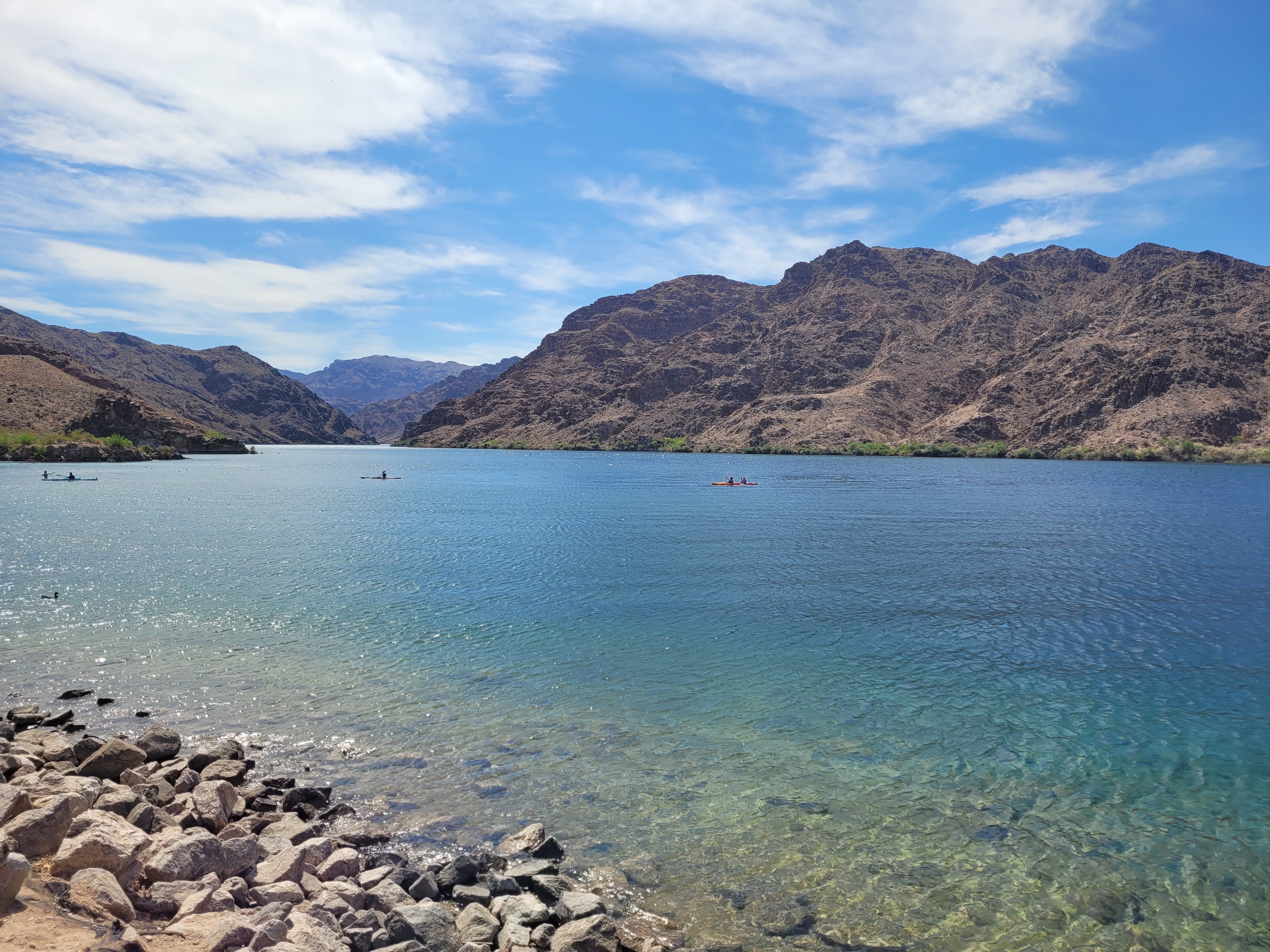 Kayakers are enjoy boating on the bright, emerald green waters of Lake Mohave in Lake Mead. The Black Canyons are surrounding the shores of the Colorado River and the sky is bright blue