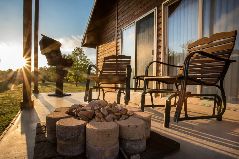 Deck of cabin with two chairs, gas grill and gas campfire.