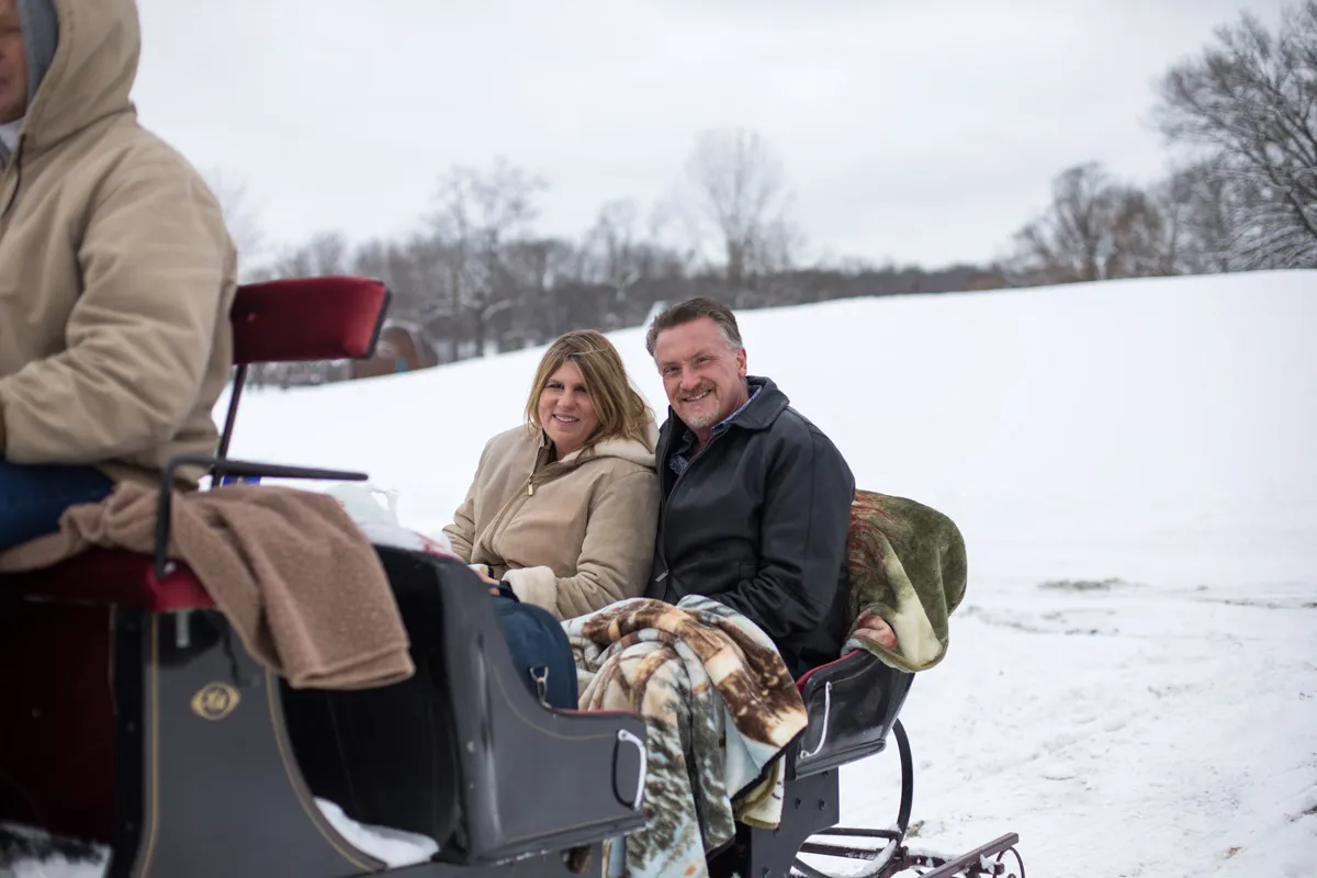 A man & woman enjoy a horse drawn carriage ride through the snow.
