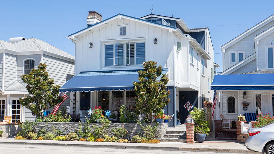 Exterior street view of the white and navy beach house at 220 Collins with a blue awning and landscaped entry
