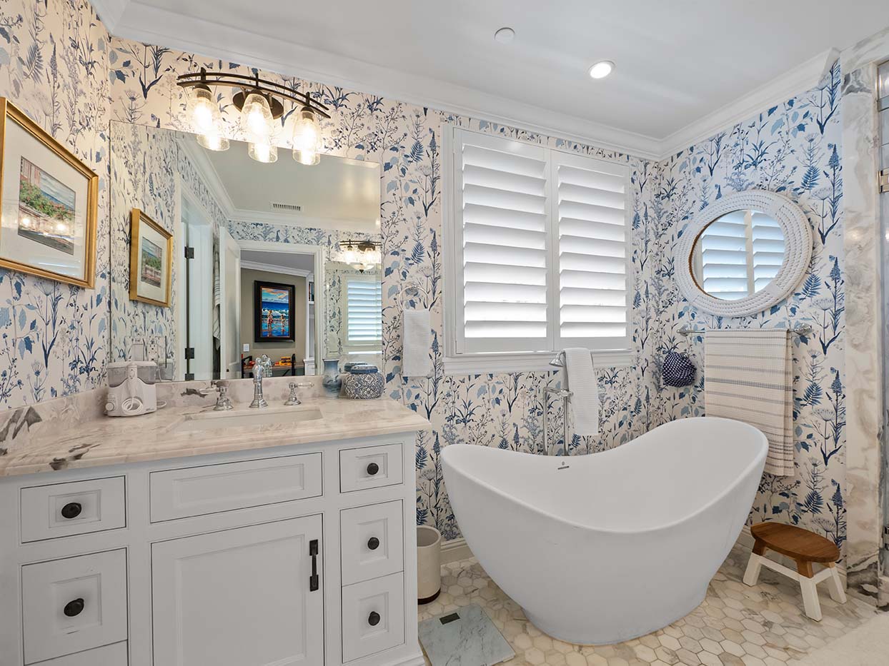 Bathroom at 220 Collins with blue botanical wallpaper, a freestanding soaking tub, and a round rope-frame mirror