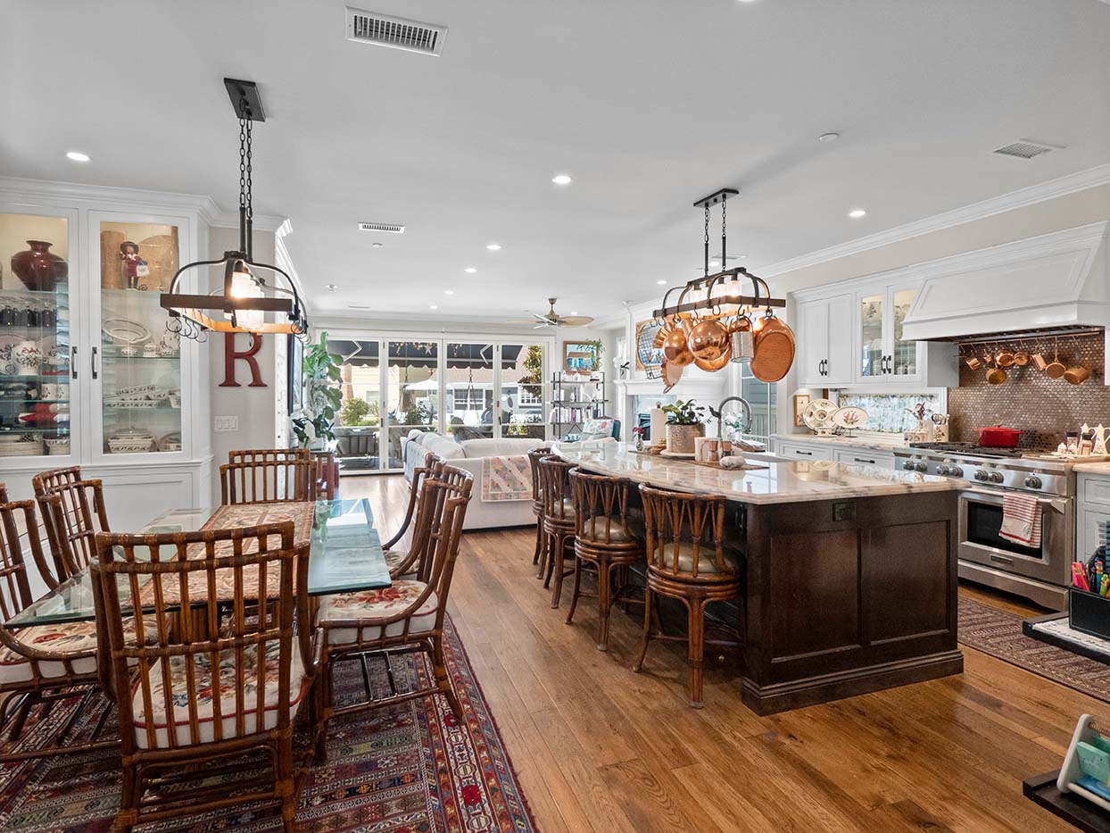 Open-concept kitchen and dining area at 220 Collins with a dark wood island, hanging copper cookware, and rattan chairs