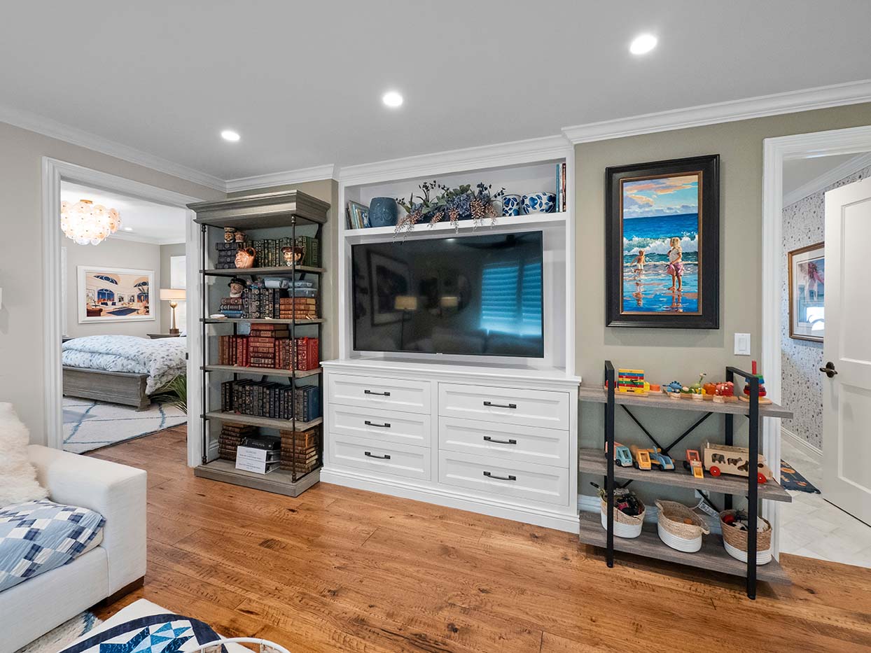 Media nook at 220 Collins with a built-in TV cabinet, bookshelves, and beach-themed artwork
