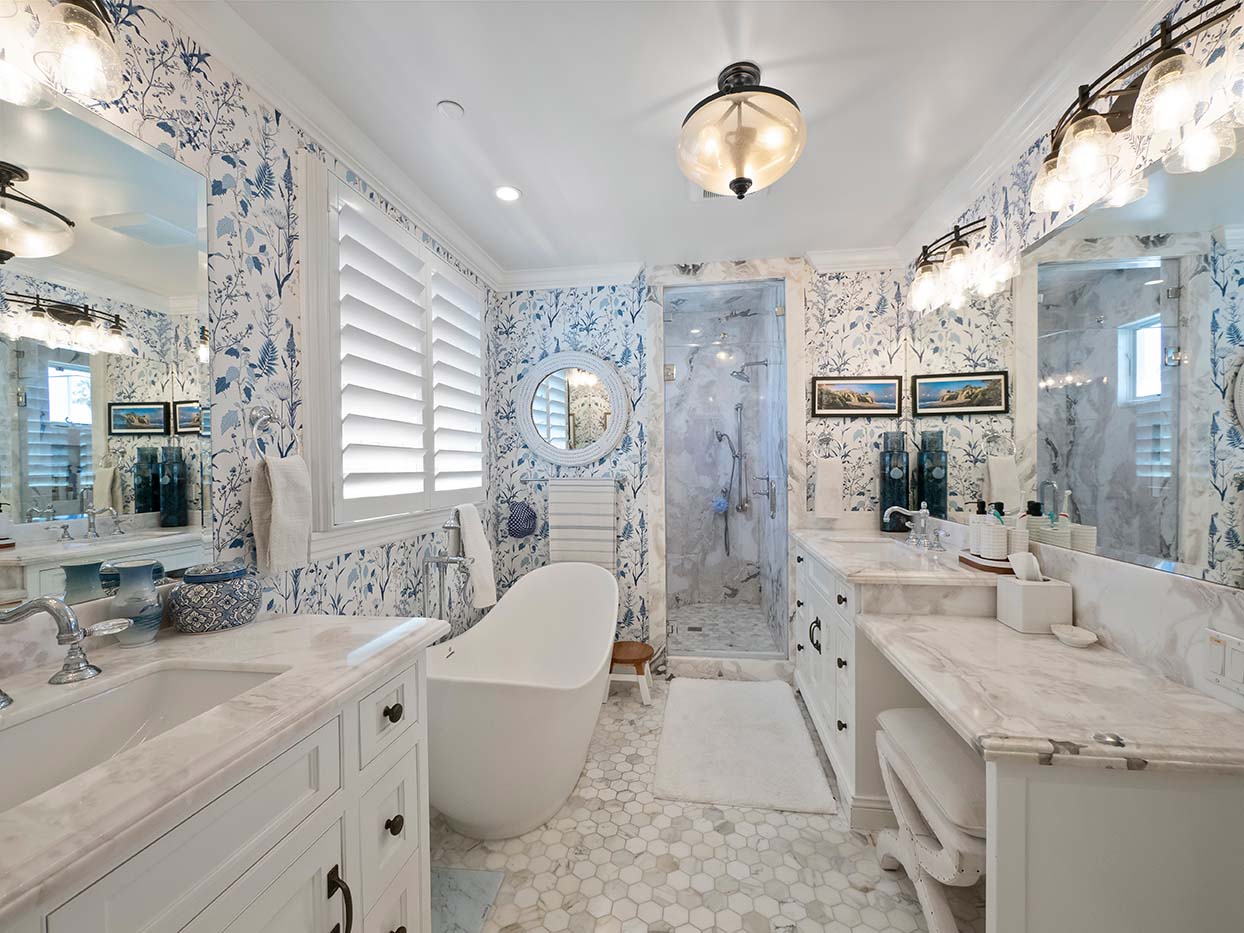 Primary bathroom at 220 Collins with blue floral wallpaper, dual marble vanities, a freestanding tub, and a glass shower