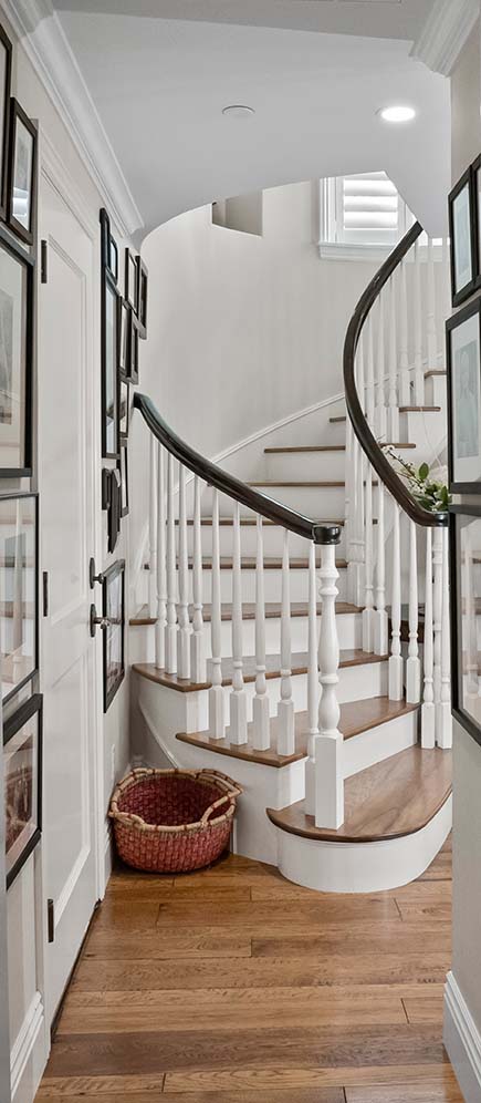 Curved staircase in the entryway at 220 Collins with a dark wood handrail, white balusters, and a gallery wall of framed photos